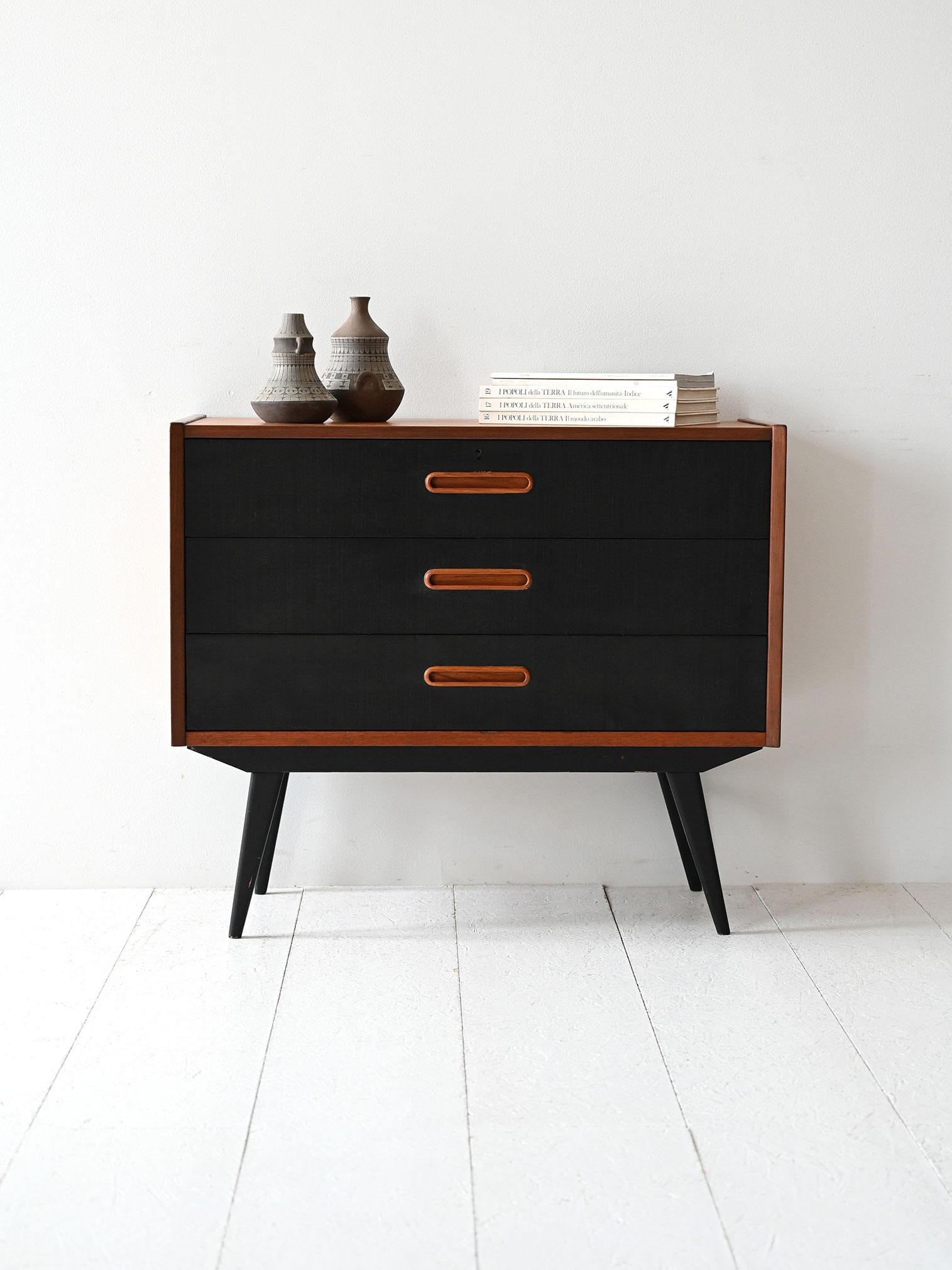 Cassettiera vintage a tre cassetti, linee pulite, gambe inclinate e maniglie scolpite. Eleganza nordica senza tempo.

Cassettiera vintage scandinava degli anni 60, con struttura in teak e frontali dei cassetti dipinti in nero a contrasto. Tre
