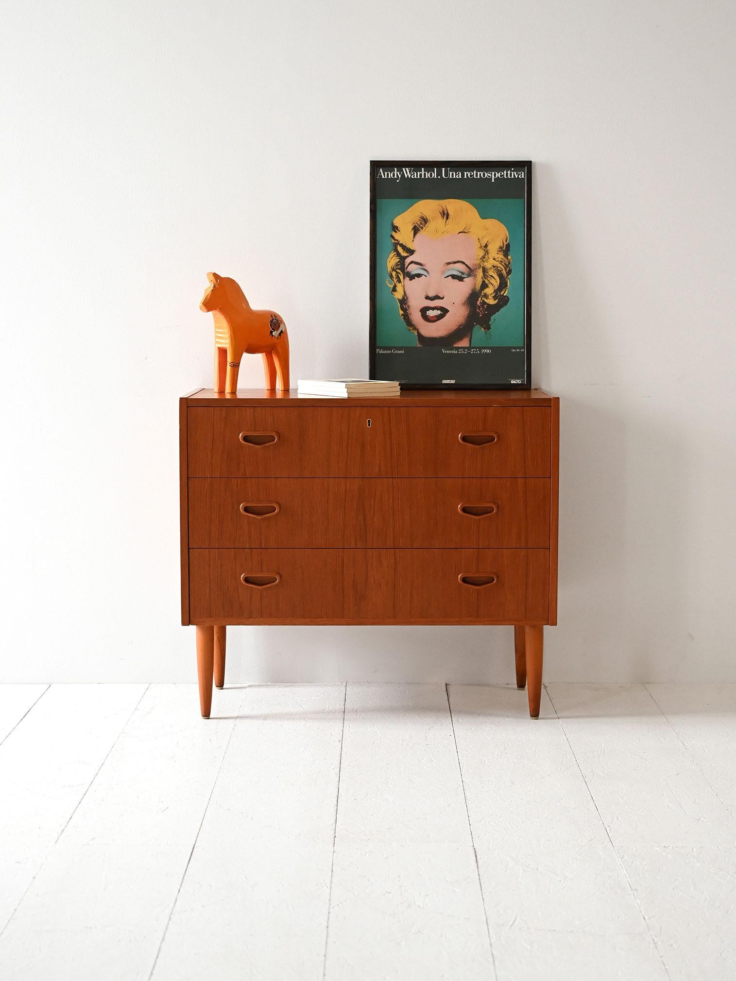 Cassettiera vintage in teak con tre cassetti e maniglie intagliate arrotondate, tipica del design scandinavo anni ’60.

Eleganza sobria per una cassettiera scandinava anni ’60 in teak, composta da tre ampi cassetti con maniglie intagliate dalla