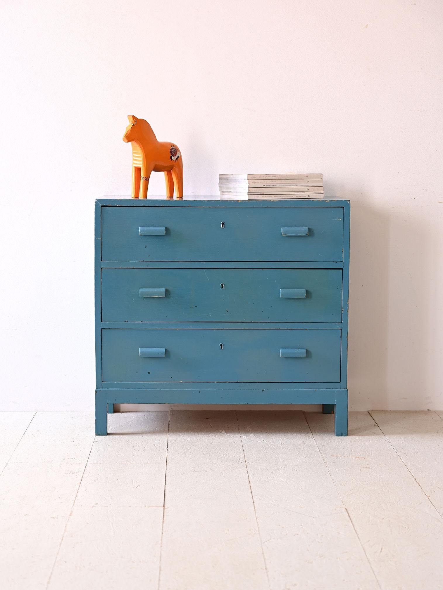 Hellblau lackierte Vintage-Kommode mit geschwungenen Holzgriffen.

Diese Möbel verkörpern den verspielten und farbenfrohen Geist des Vintage-Designs und machen jeden Raum heller und einladender.
Die Kommode hat einen massiven Holzrahmen, der in