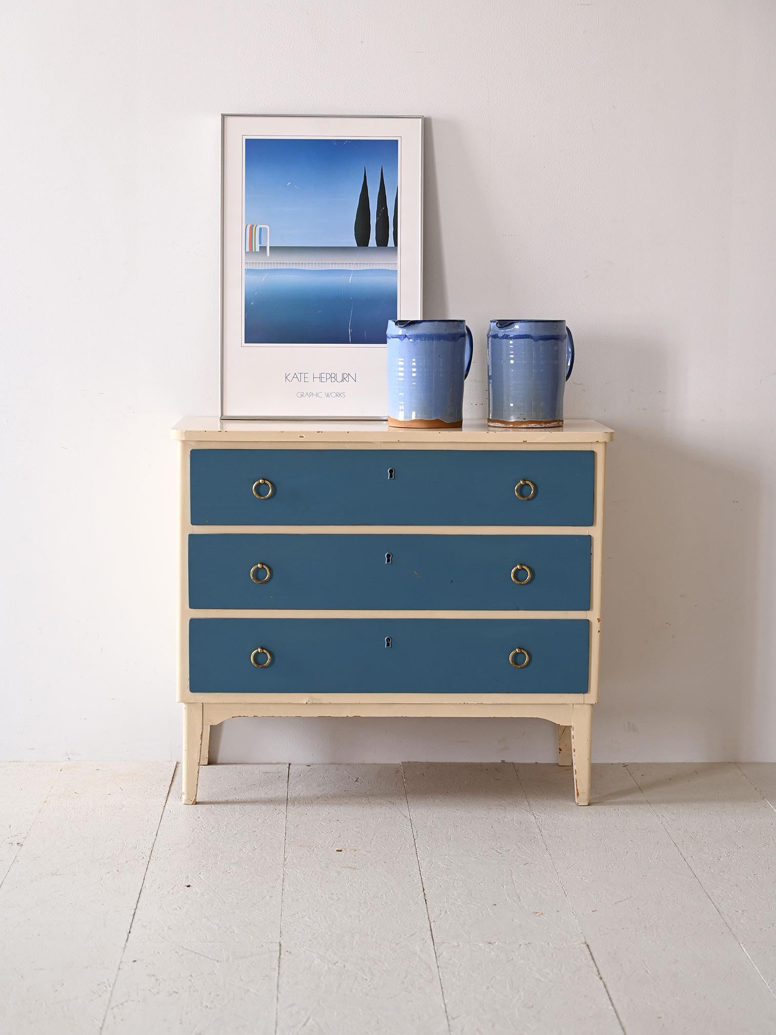Retro cabinet with three drawers and gold metal handles.

With its vibrant shades of blue and white, this chest of drawers brings a breath of freshness and originality. Its compact silhouette, enhanced by slender Nordic-style legs, fits discreetly