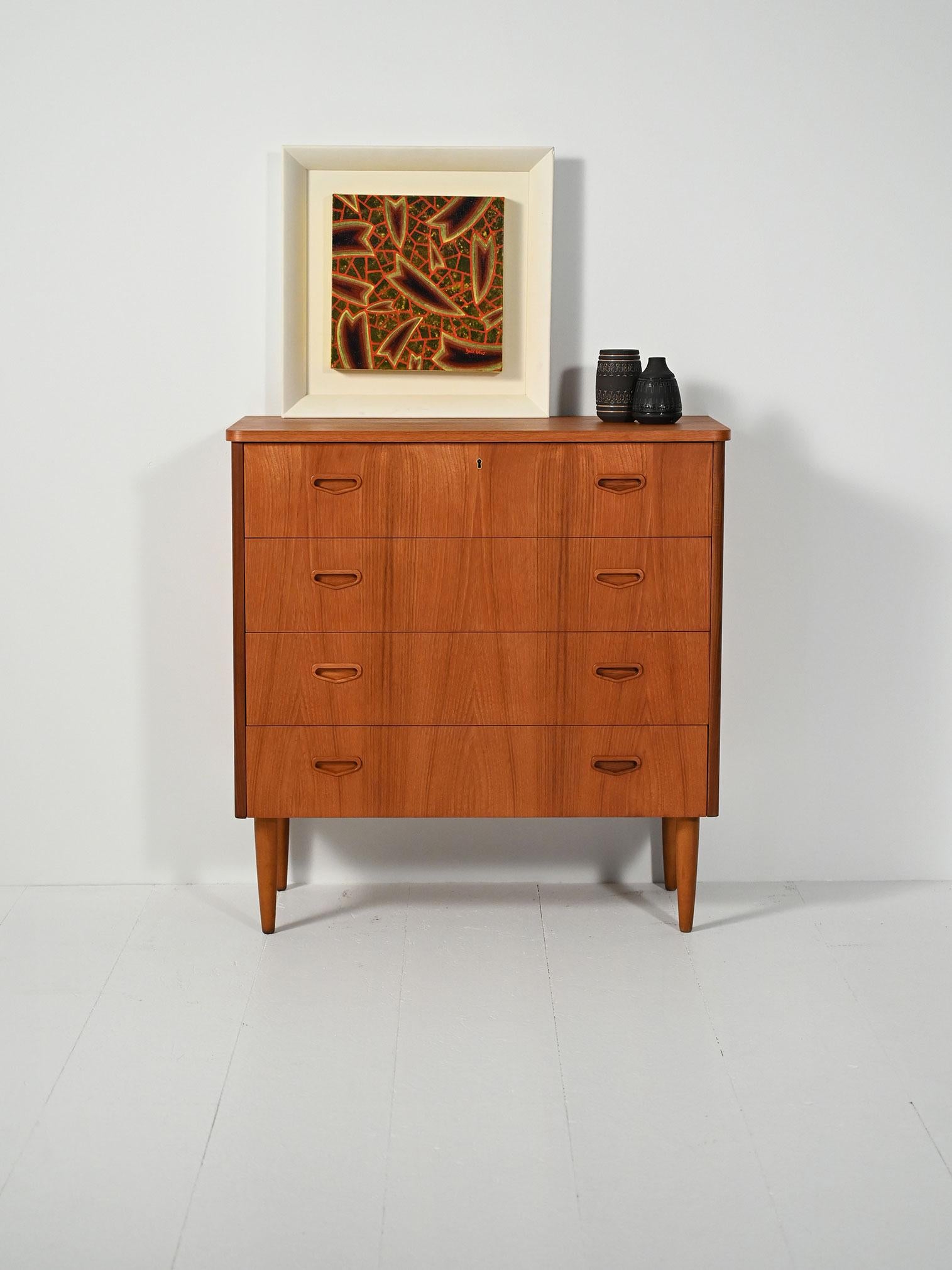 Cassettiera scandinava anni 50/60 in teak, quattro cassetti, maniglie incassate scolpite e gambe tornite svasate. Linee essenziali, venatura calda.

Cassettiera in teak dei tardi anni '50/'60 con quattro cassetti allineati. Le maniglie incassate