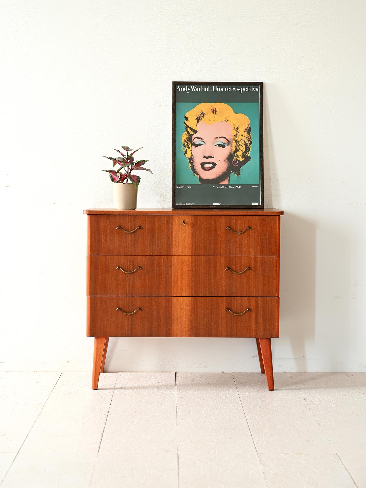 Cassettiera anni '60 in teak caratterizzata da dettagli eleganti e da una struttura solida. Il mobile presenta tre cassetti spaziosi, ciascuno con impugnature in metallo. Il primo cassetto è dotato di serratura.

Un elemento distintivo di questa