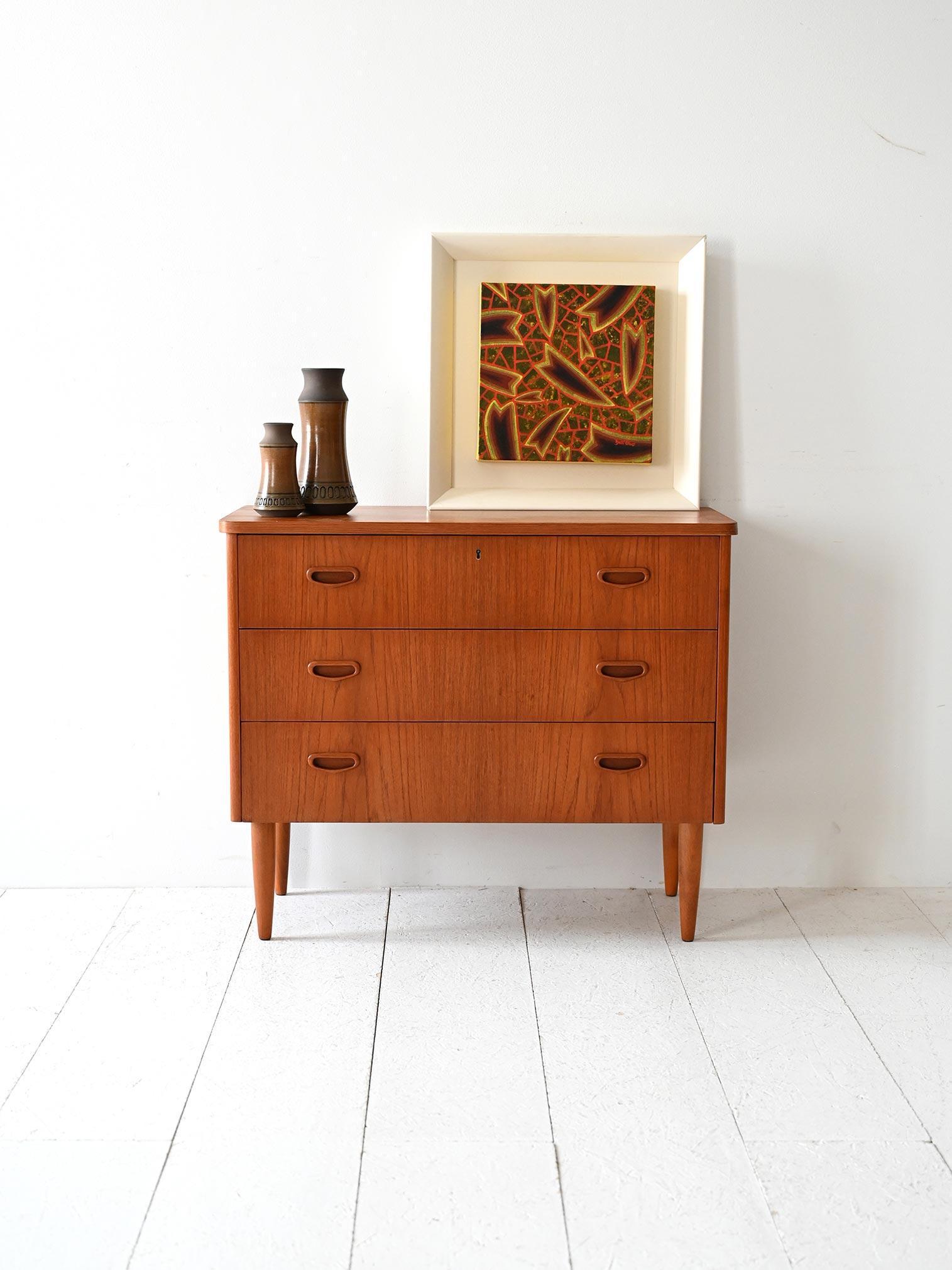 Cassettiera vintage anni ’60 con tre cassetti, maniglie intagliate e gambe sottili tornite, in stile scandinavo essenziale.

Cassettiera scandinava originale anni ’60 in teak, composta da tre cassetti con maniglie intagliate dalla forma organica e