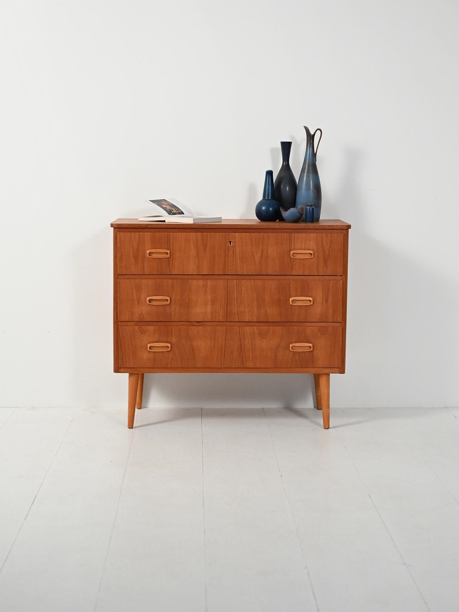 Cassettiera anni ’50–’60 in teak con dettagli in rovere: tre cassetti con doppia maniglia incassata e gambe tornite affusolate. Linee leggere, sobrie.

Elegante cassettiera scandinava in teak con profili e maniglie in rovere, tre cassetti con prese