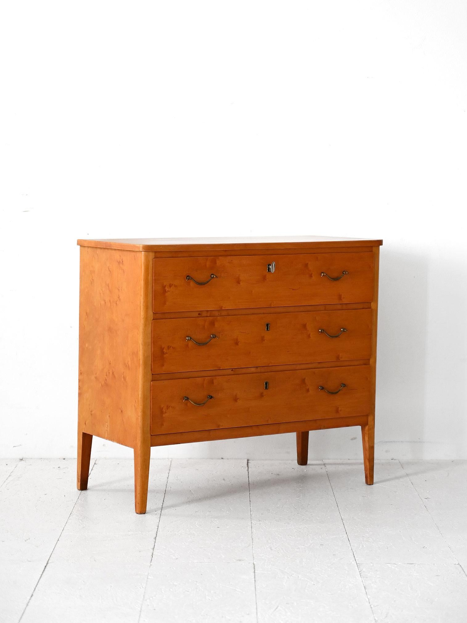 Commode du milieu du siècle à trois tiroirs avec serrure à clé, en bouleau. Lignes épurées et détails métalliques.

Commode scandinave vintage en racine de bouleau, avec trois tiroirs et une serrure à clé. La structure a un design discret avec des