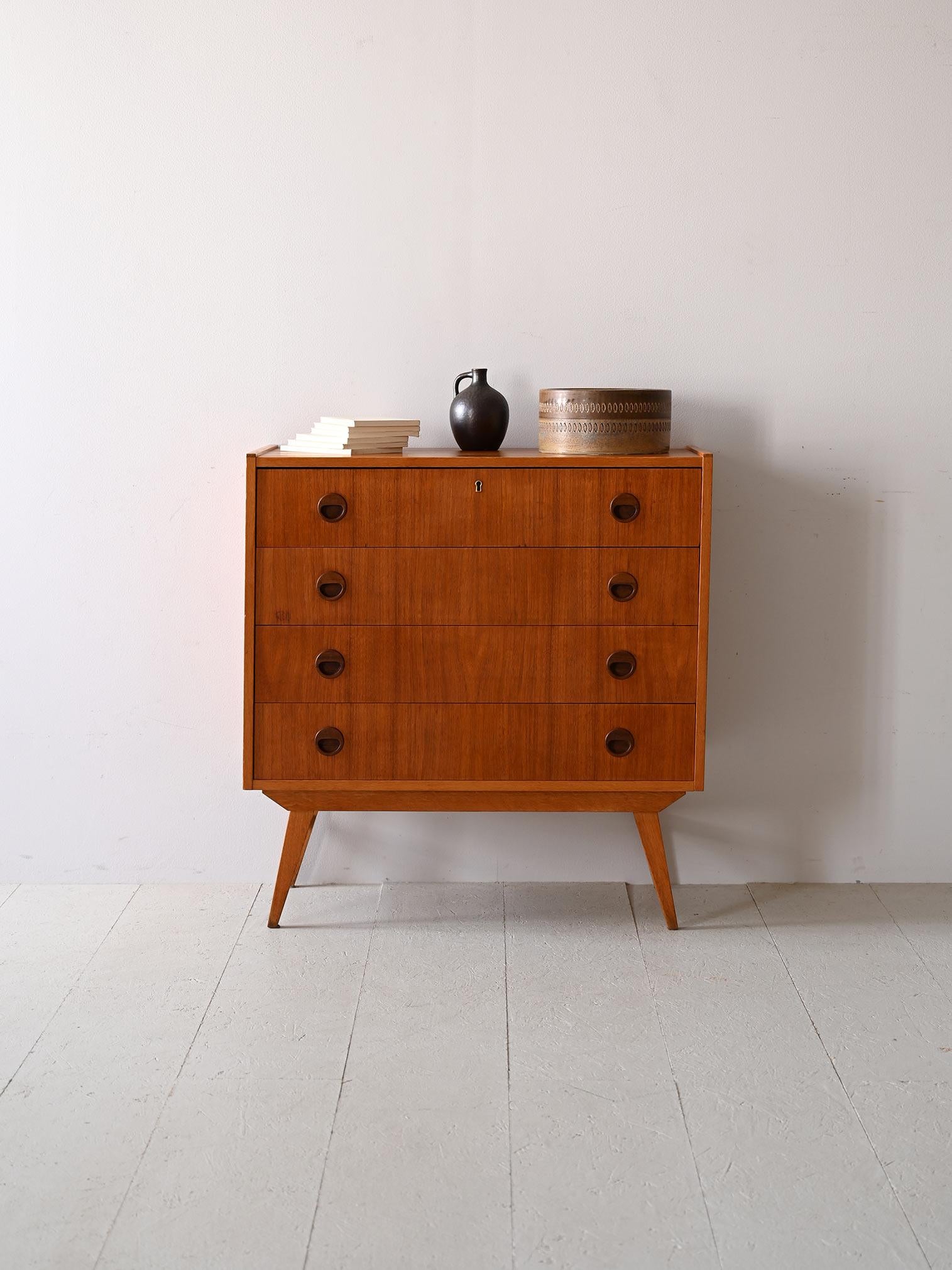 La cassettiera, originaria del design nordico anni '60, è realizzata in teak, un legno apprezzato per la sua resistenza e la grana distintiva.
Il suo aspetto è definito da linee semplici e maniglie tonde incassate, tipiche dello stile del tempo. Pur