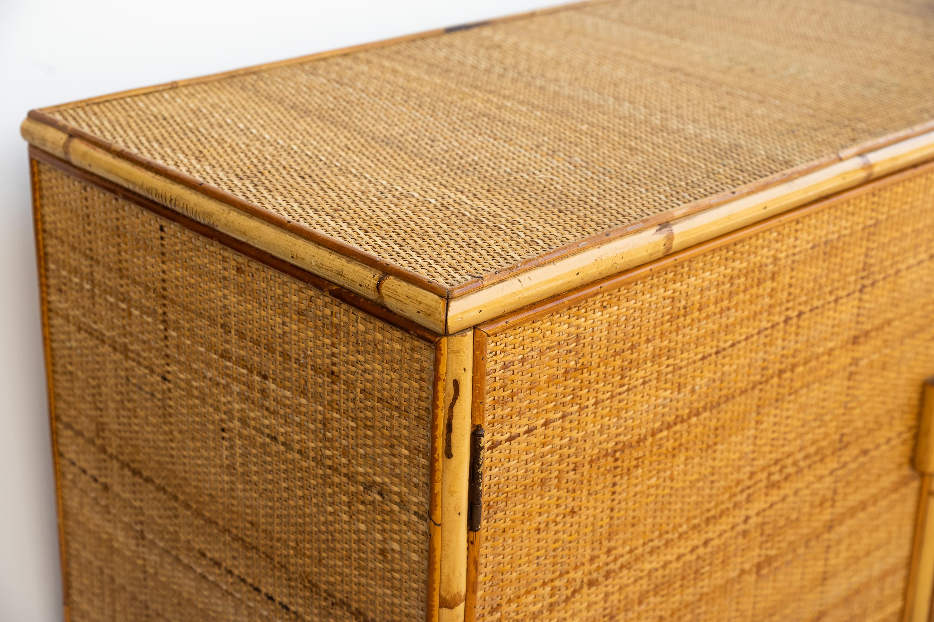 Questa bellissima cassettiera vintage in vimini e bambù risale all'anno 1970.  
E' realizzata in legno rivestito da una trama in rattan e le maniglie sono rivestite in giunco. Ha due sportelli e quattro cassetti in vimini e bambu'. 
Prodotto in