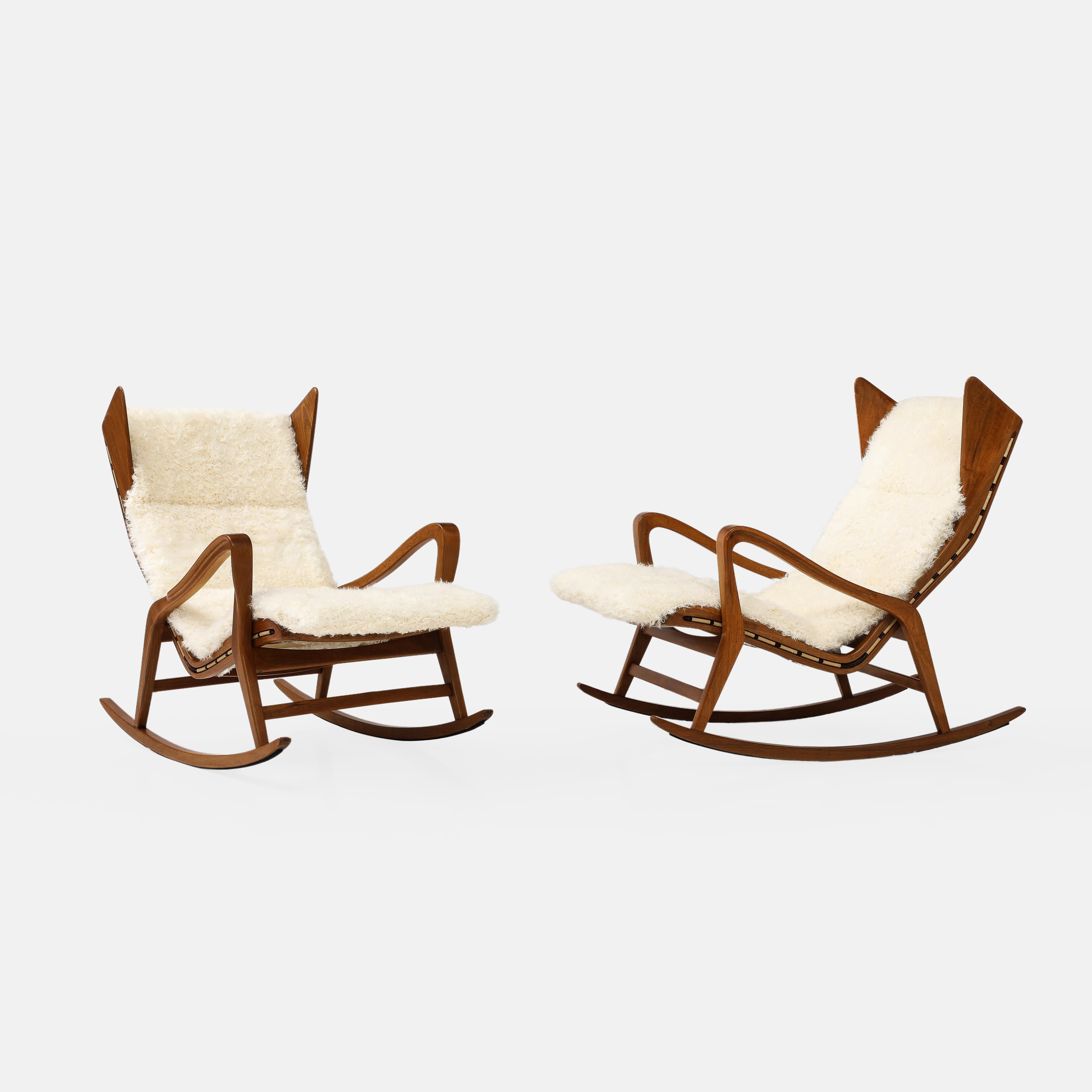 Cassina, sculptural walnut rocking lounge chairs model 572 with ivory Kalgan lambskin channeled cushions on Pirelli webbing, Italy, 1955.  These exquisite modernist rocking chairs have exquisite detailing throughout including finely carved walnut