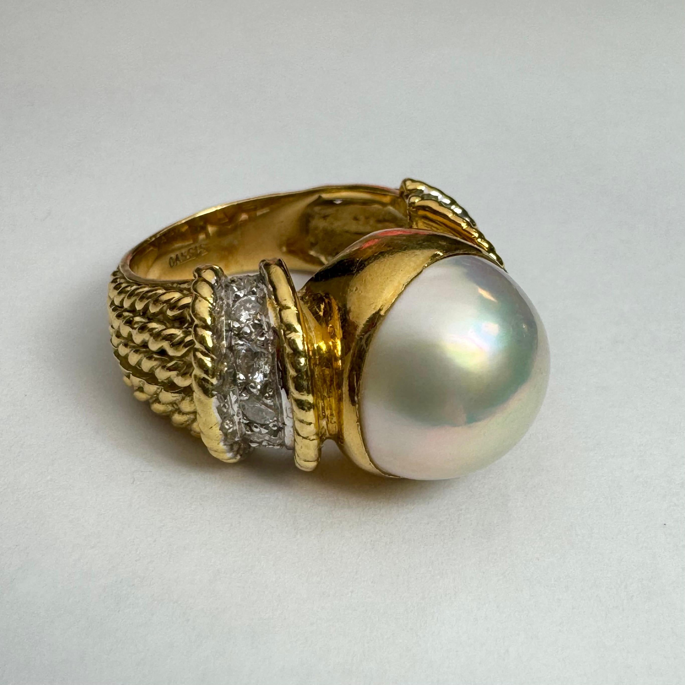 Stately and elegant, the stunning cocktail pearl and diamond ring in 18k yellow gold, by designer CASSIS. In the center sits a large white cultured pearl that measures 13.4mm. There are 5 white, round brilliant cut diamonds on either side of the