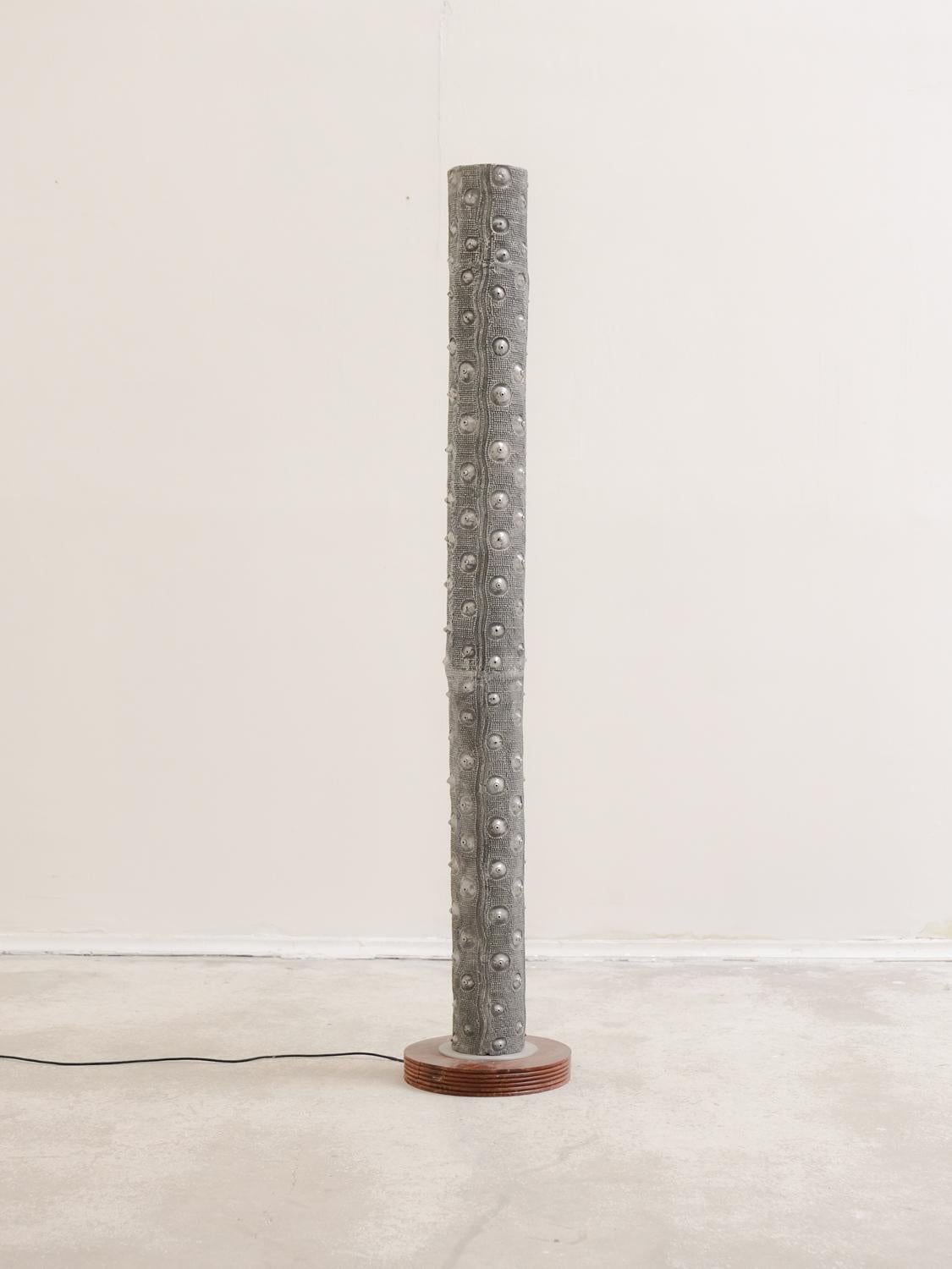 Floor lamp presented as a light column with cast aluminium nipples resting on a round wooden base, anonymous work from the 1990s.

This imposing luminous column with an offbeat aesthetic is like a real functional sculpture. The texture is put to