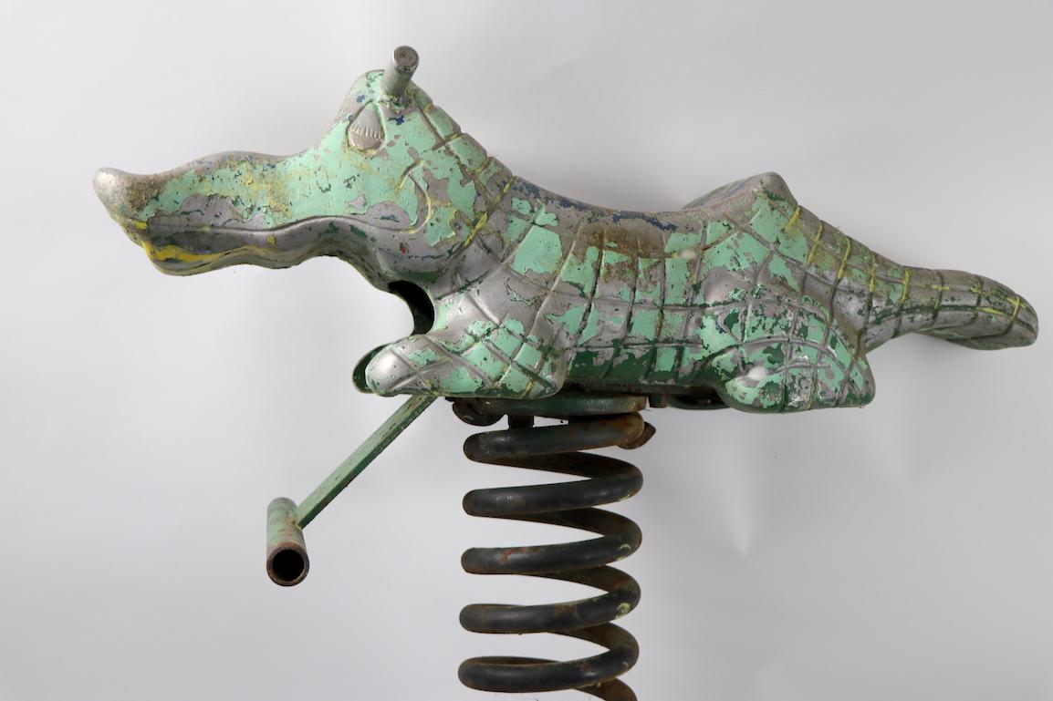 Cast aluminum ride on toy alligator, made by Mexico Foundries Reedsville Pennsylvania. This example is in nice original condition with patinated paint surface. The base is a coil spring, welded to a long iron bar, which was originally countersunk