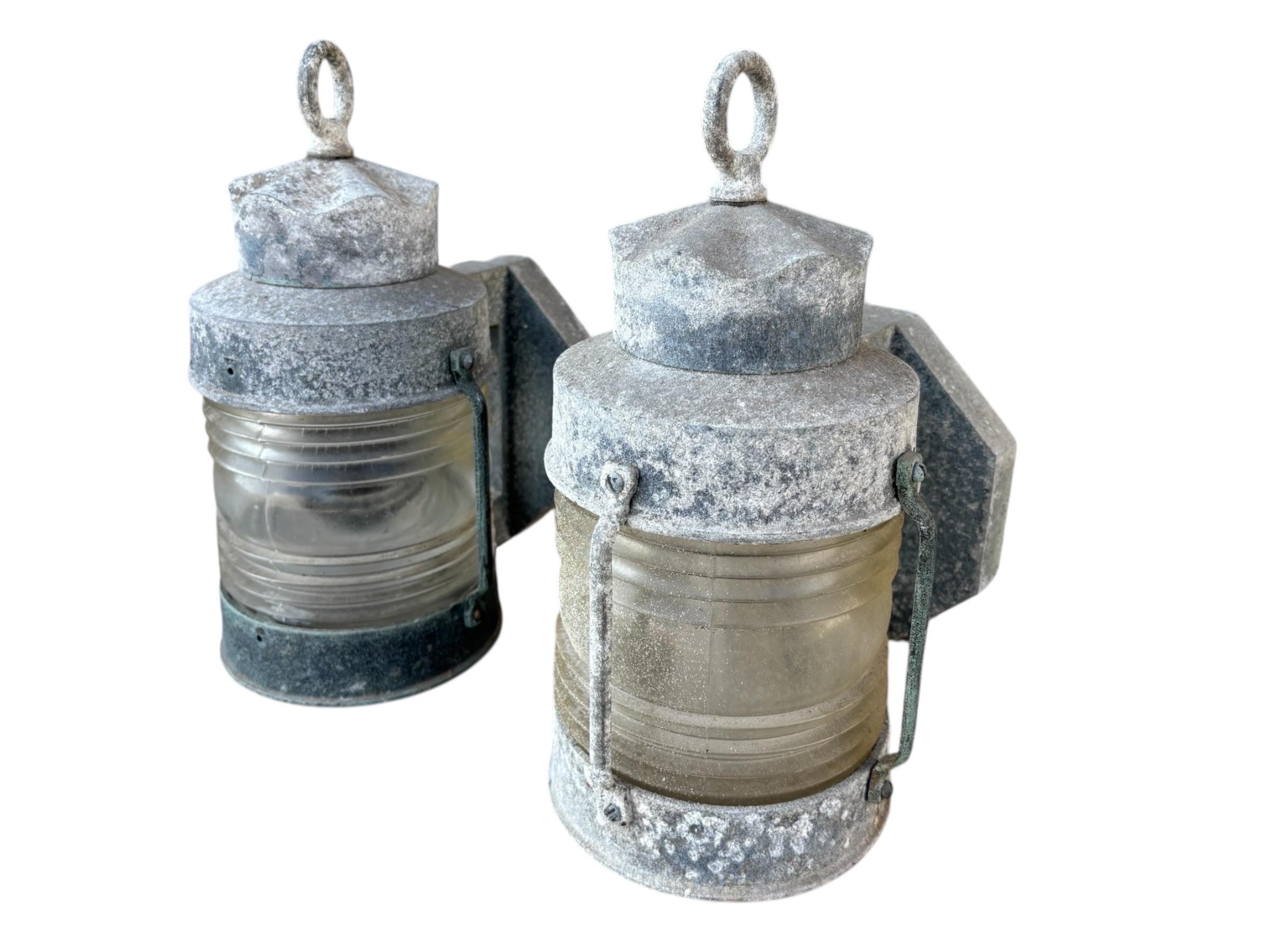 A pair of nautical wall mounted masthead lanterns circa 1960. Made of cast aluminum with rich patina, ribbed glass chimneys and octagonal back plates. Serpentine cap is topped with a hoop finial to give the look of a hanging lantern.