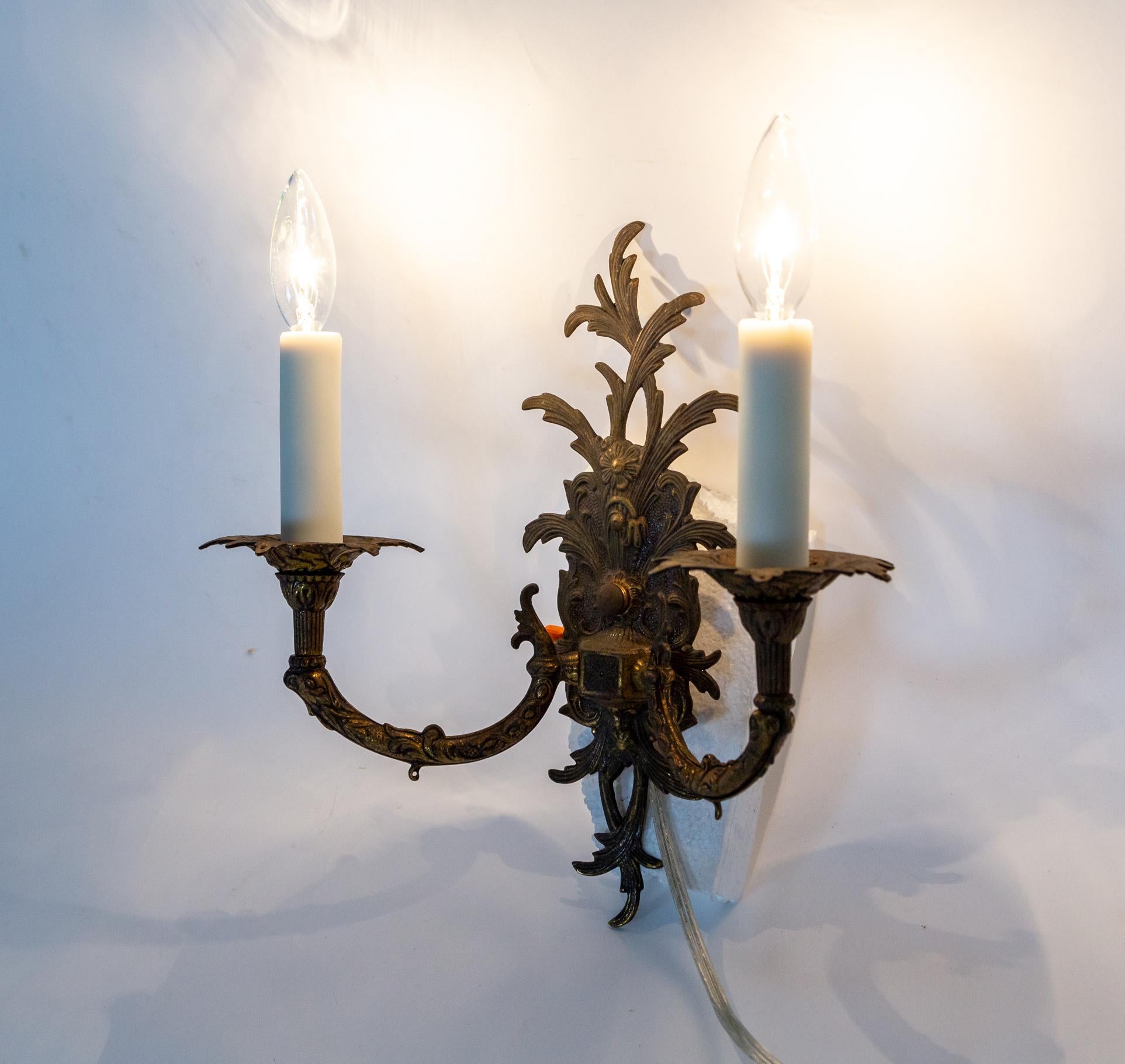 Aplique antiguo de latón macizo con forma orgánica y una rica pátina oscura. Del soporte de pared fundido brotan hojas de acanto con dos detallados brazos de candelabro, bobos y detalles florales. Nuevos cubrevelas de resina marfil. Principios de