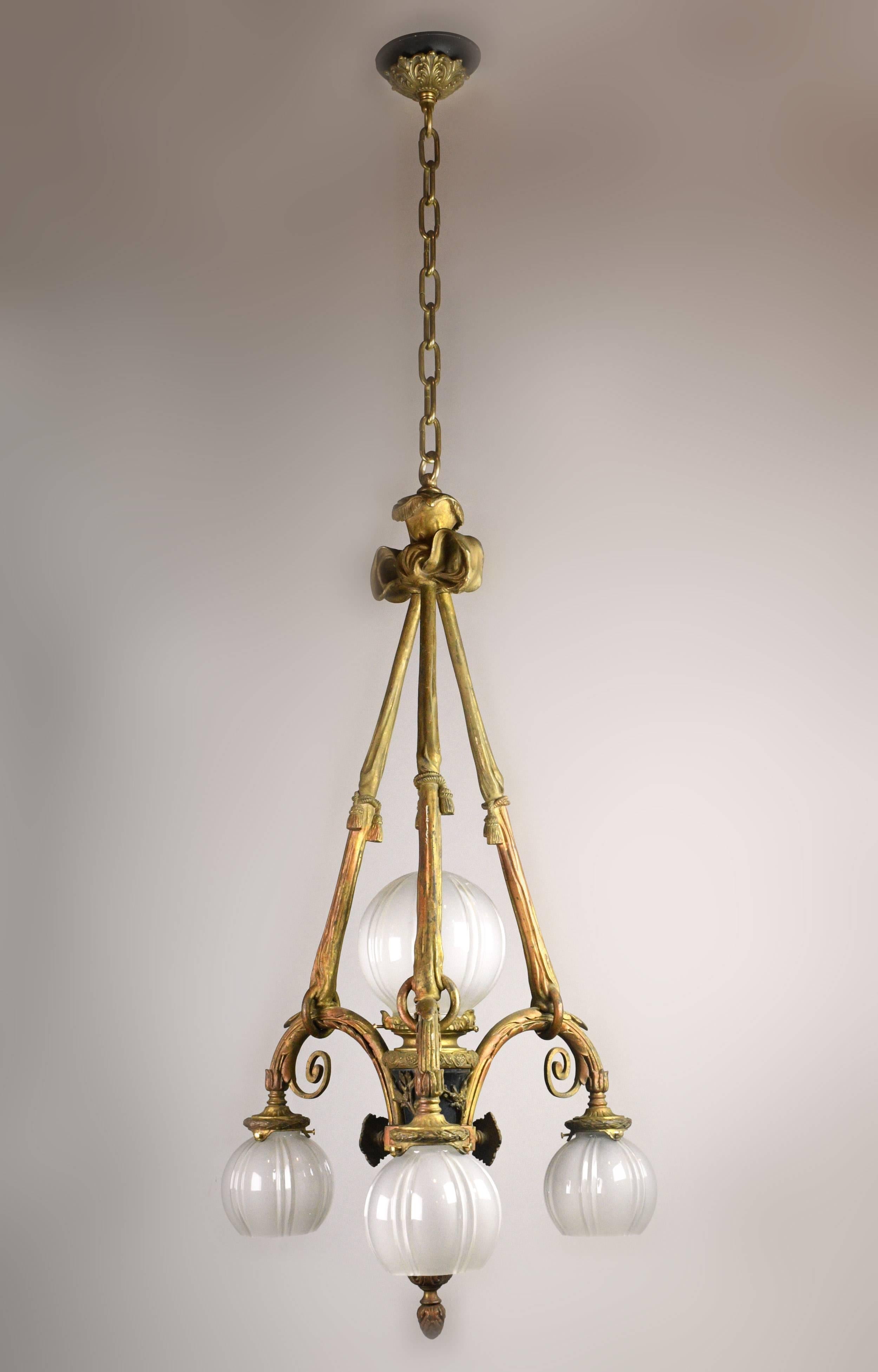 Incredible cast brass Beaux Arts style four shade chandelier with shimmering gold, orange, and black details. The body of the chandelier features heavy organic ornamentation; large floral “buttons” jut out from all three sides, while curving twigs