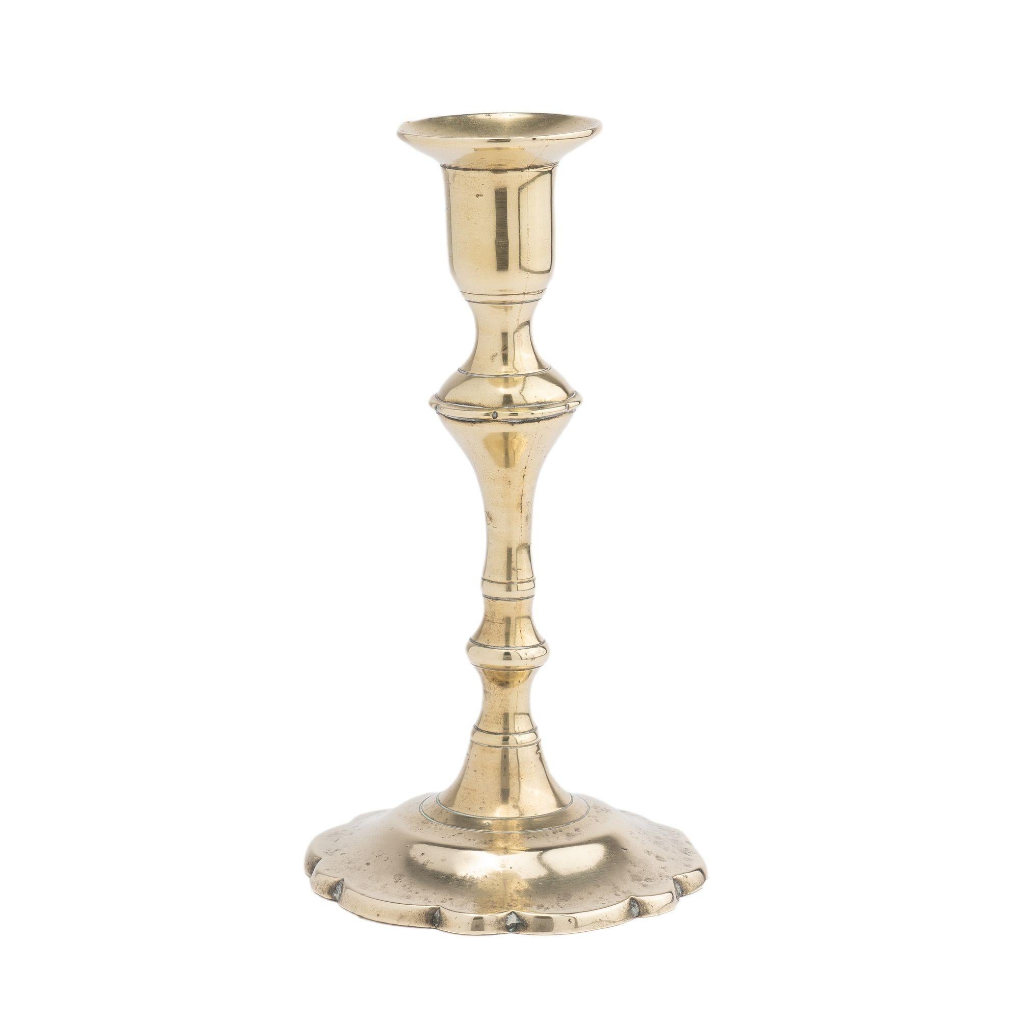 A rare miniature form of seam cast brass Queen Anne petal base candlestick with urn form candle cup. The candlestick has been cast with a bobeche, a trumpet form shaft with suppressed knob peened to a conical form, and centered on dished circular