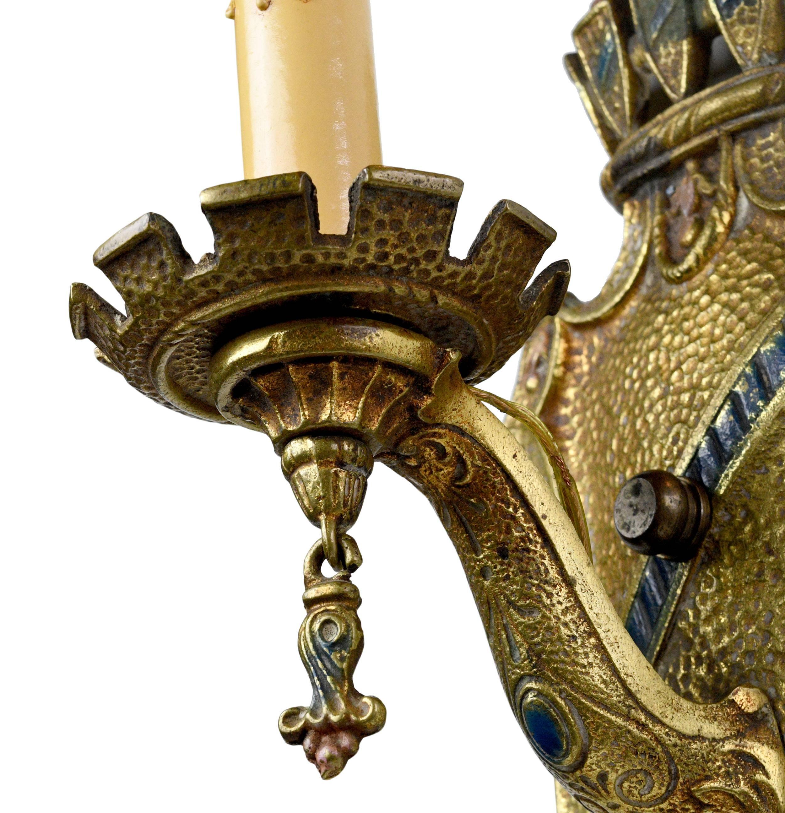 This Tudor sconce is part of a set of five matching sconces. These fixtures have an antiquated feeling due to the robust nature of the backing plate, as well as the crown that adorns the top of the sconce. With its heavy style, this fixture is a