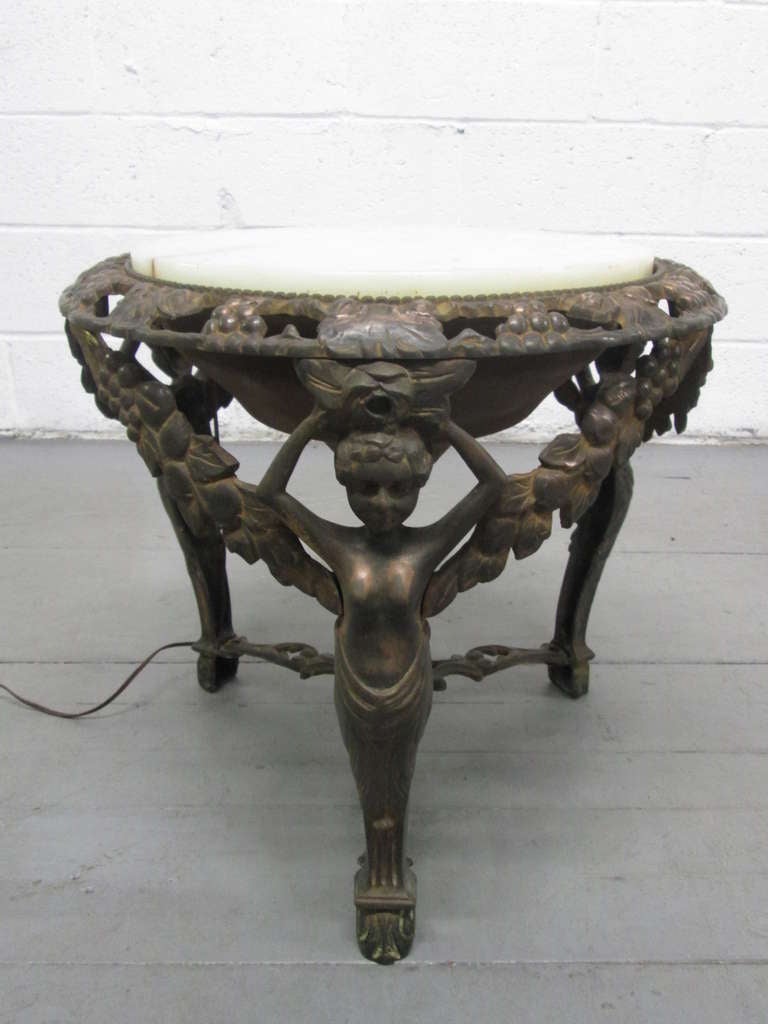 Cast bronze coffee table with an illuminated alabaster top. Table has a three figural legged base.