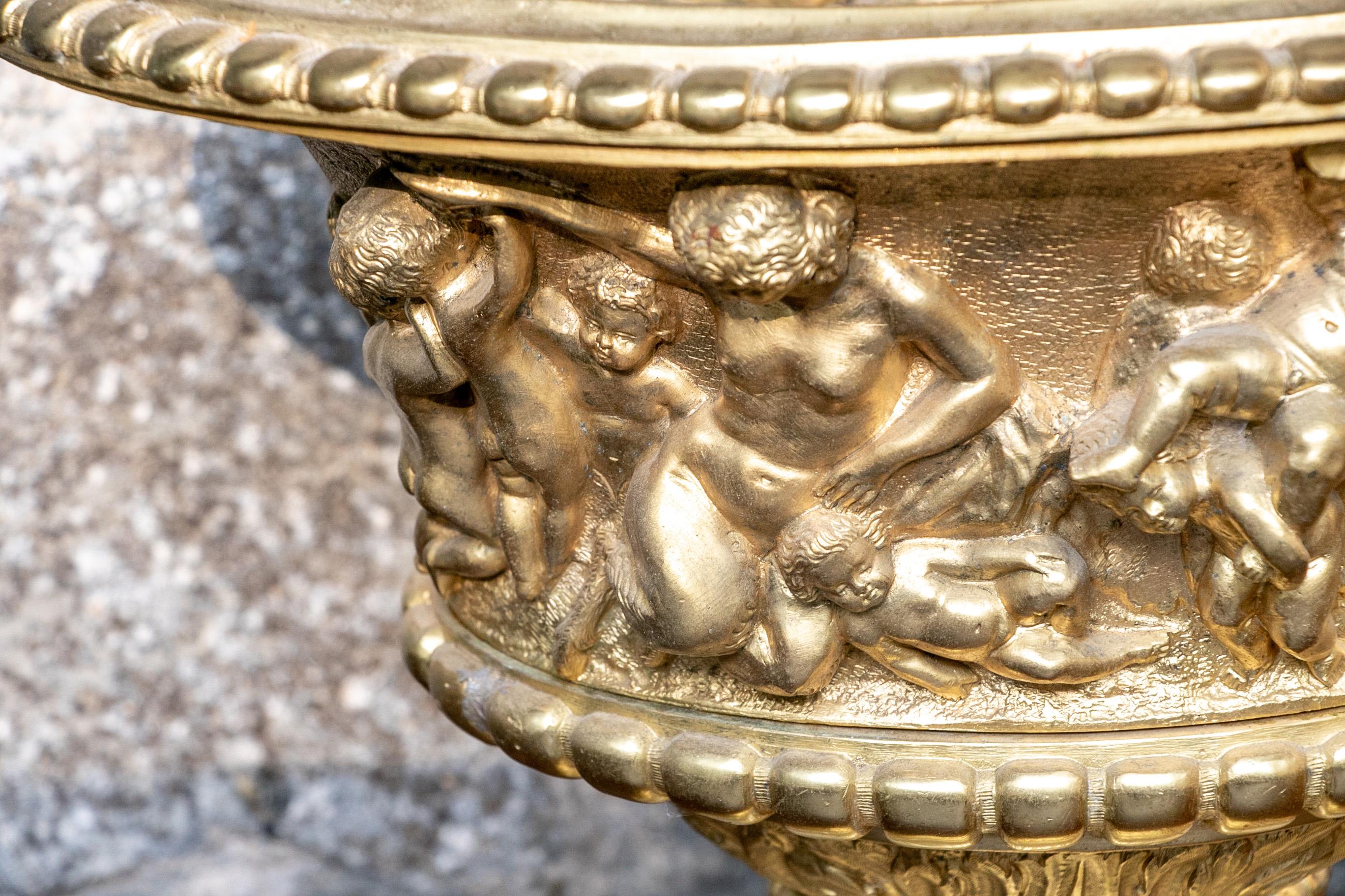Cast bronze urn form planter, oval urn with high relief decoration with Venus and a troupe of playful putti. The fluted base with a band of grape leaves. A hole in the bottom. Mounted on a tiered brass base. 

Condition: Good condition with some