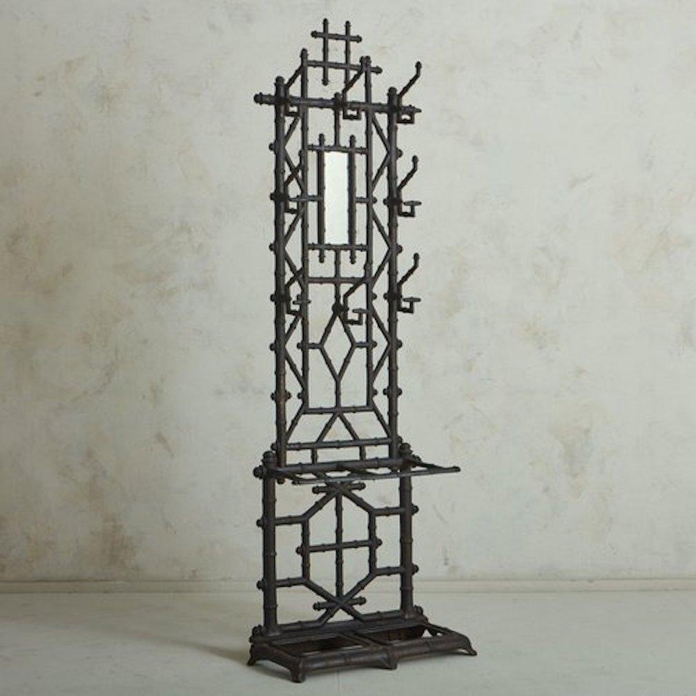 A free standing antique French patinated cast iron coat rack or hallway tree featuring a sculptural faux bamboo motif frame. This rack has eight double hooks for coats or hats, which surround an antiqued inset rectangular mirror. It has a lower