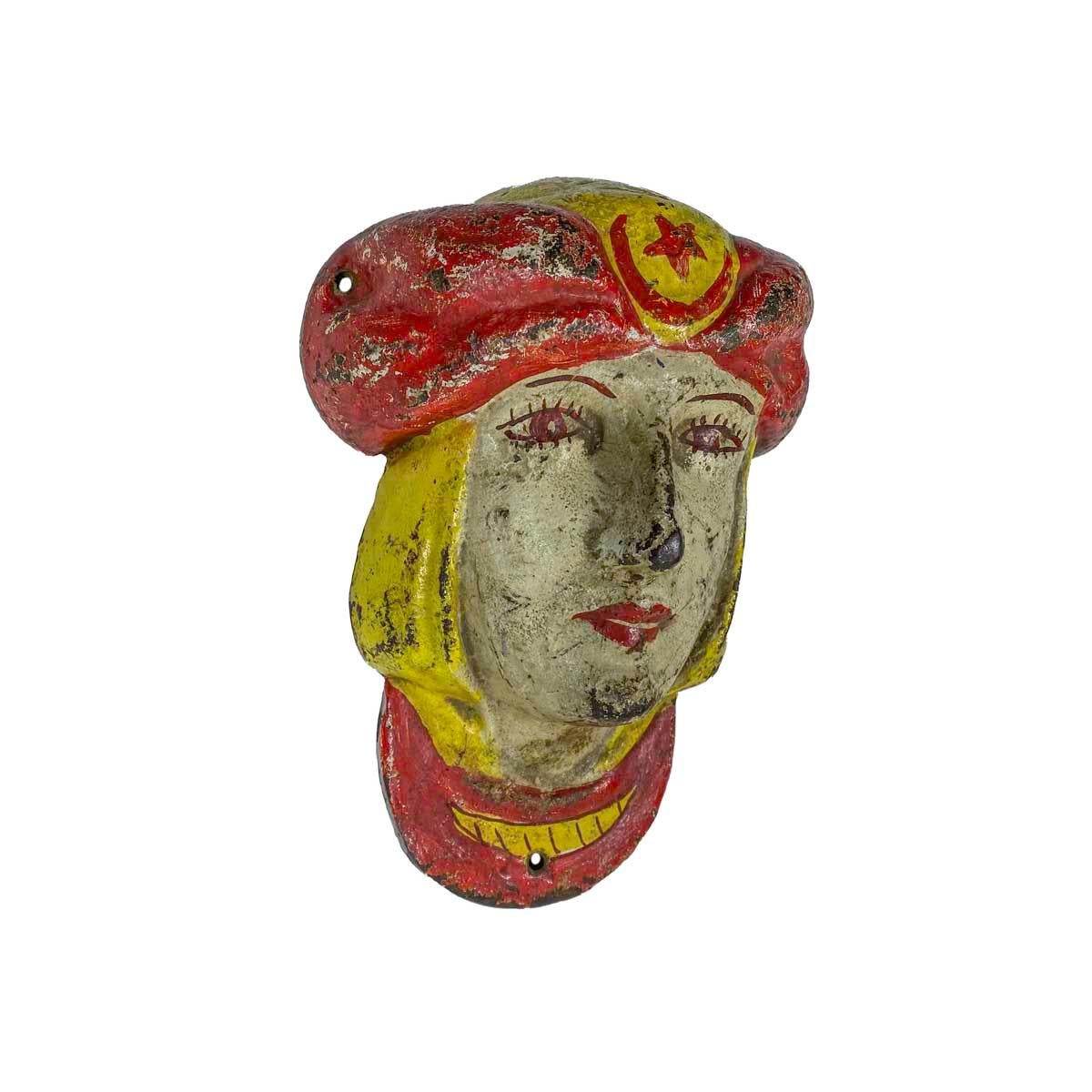 Painted cast-iron mask of a woman wearing a red turban with a star and crescent moon. Typical of amusement park and carnival art of the period it is painted in strong, bright colors, early 20th century.
  