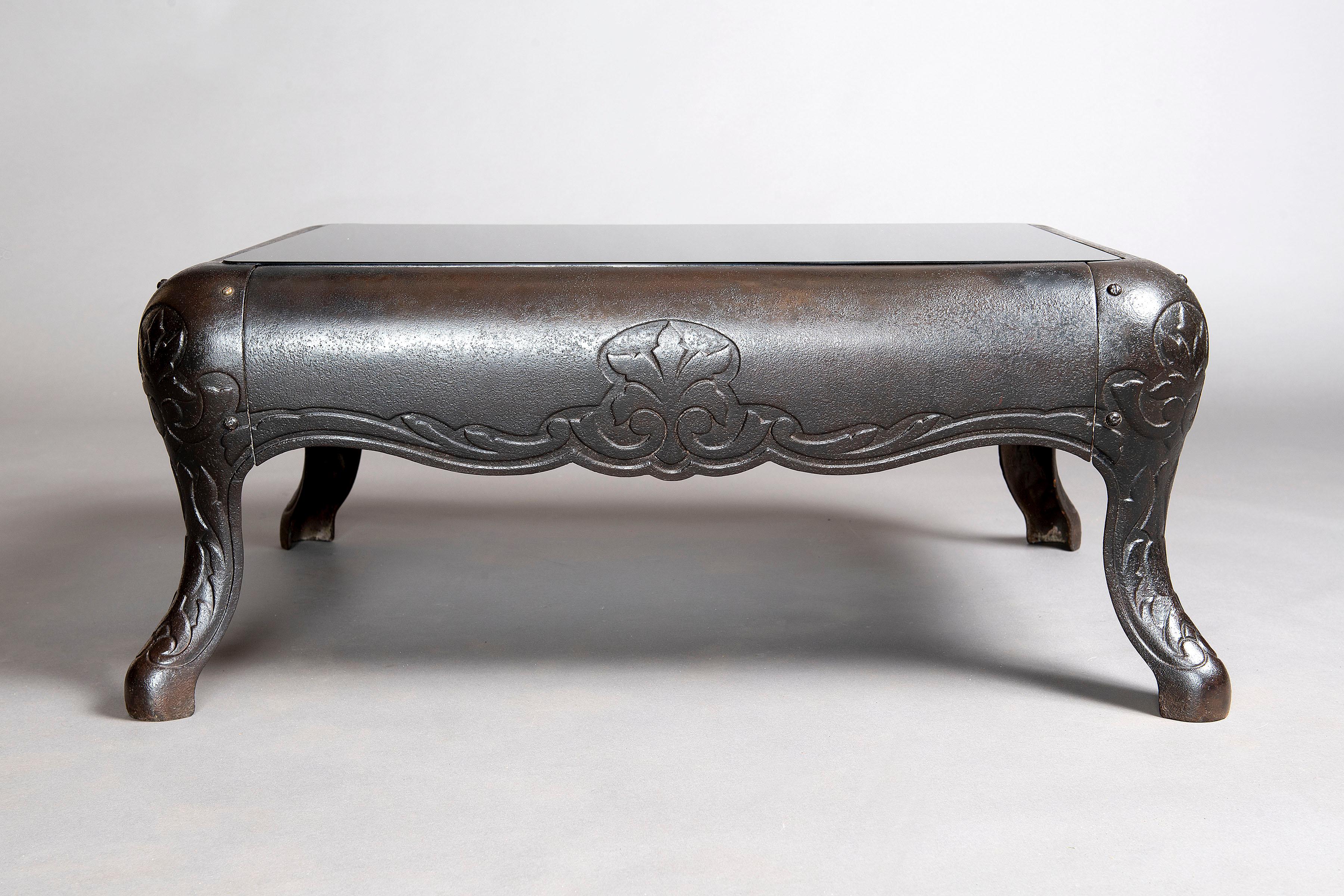 La base d'un poêle antique réutilisé a été transformée en une table basse unique en son genre avec un verre gris fumé.
La table basse en fonte s'inspire du passé et se modernise avec le verre translucide gris.