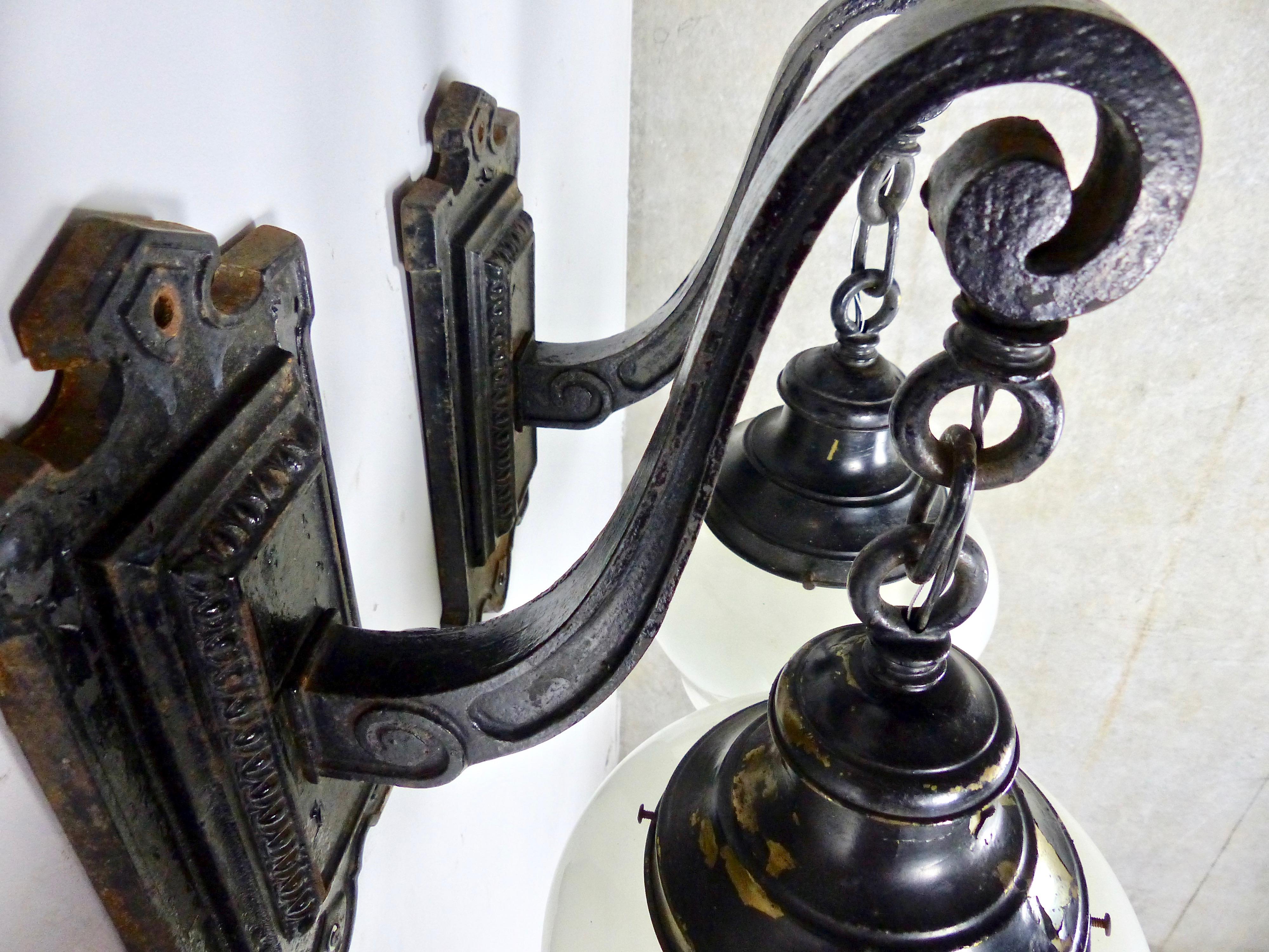 Matched pair of beautifully proportioned exterior wall sconces, circa 1900. Nice details in the decorative cast iron. Early schoolhouse-style glass globes. Shade Fitters are oxidized black paint over brass.
 Re-wired and CSA approved. Dimensions 21