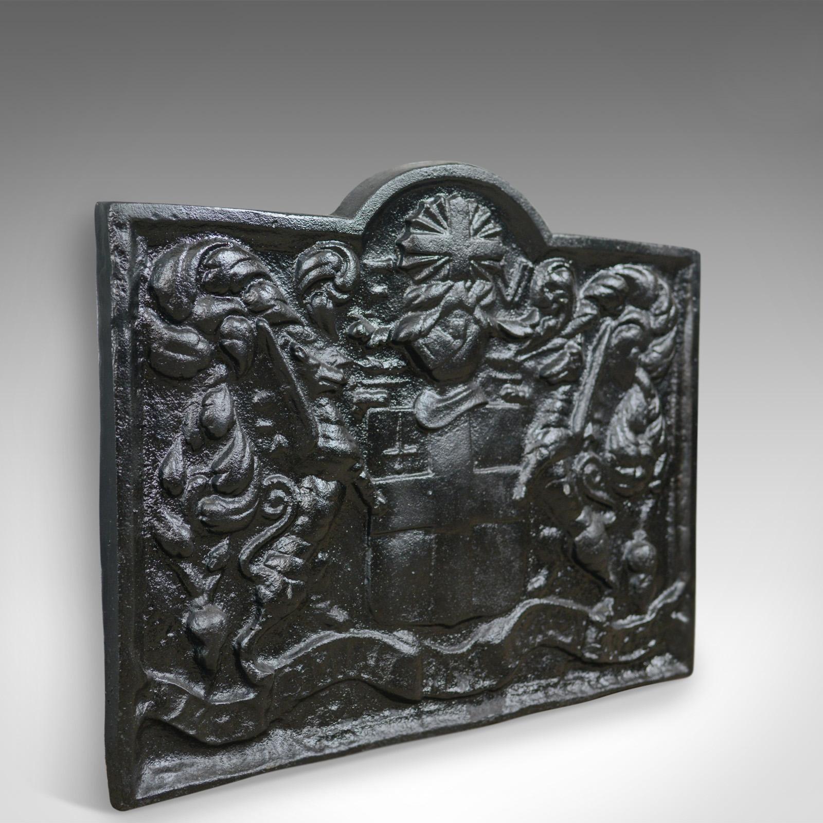 This is a cast iron fire back from the early 20th century displaying a coat of arms.

Heavy fire back in cast iron with a blackened finish
Shaped top over oblong plate
Casting of the coat of arms supported by beasts
Crest with cross and