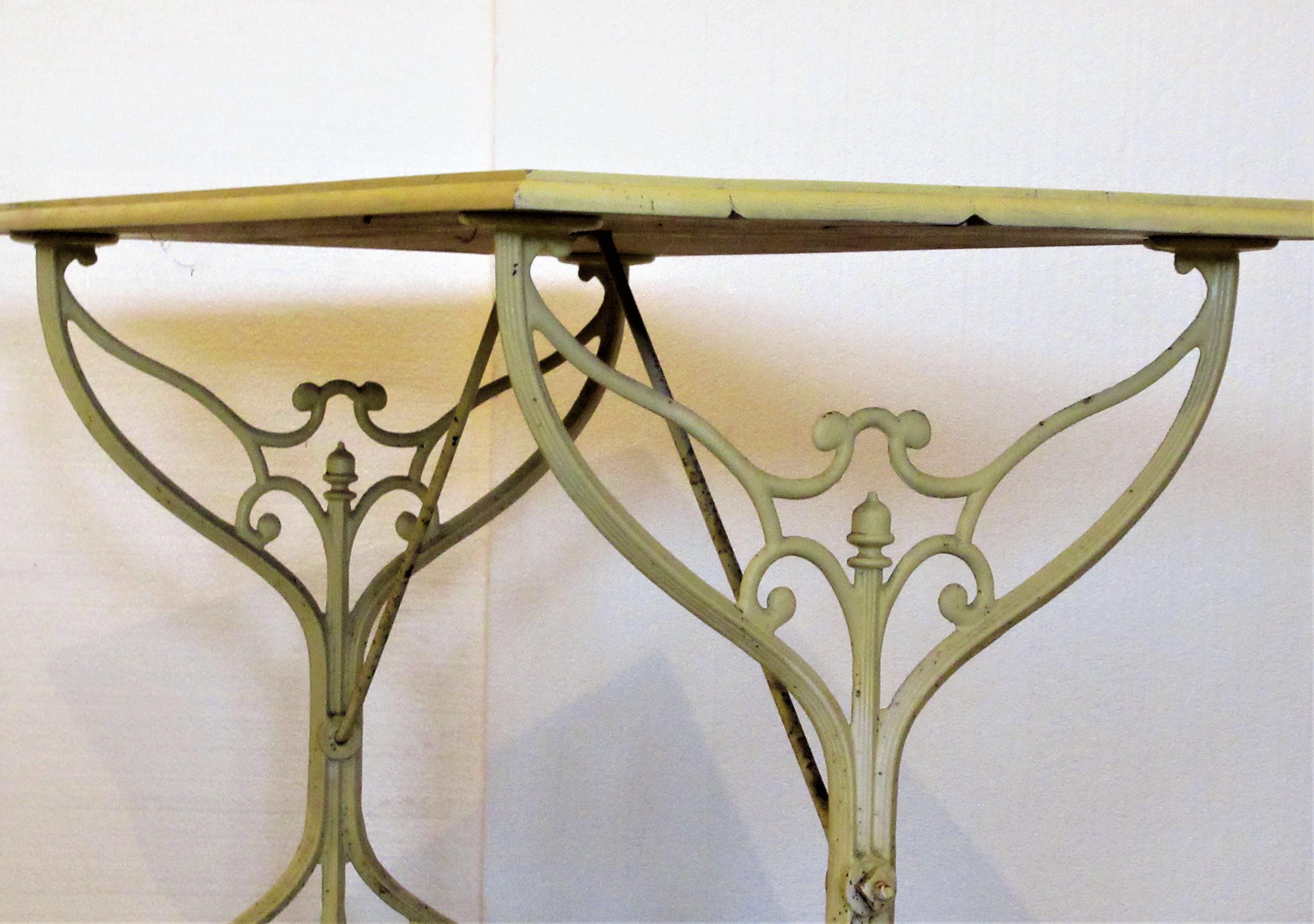 Antique cast iron gothic style base garden bistro table with a shaped wood top - all in pale yellow painted surface. Most likely French in origin dating from the earlier part of the twentieth century. Look at all pictures and read condition report