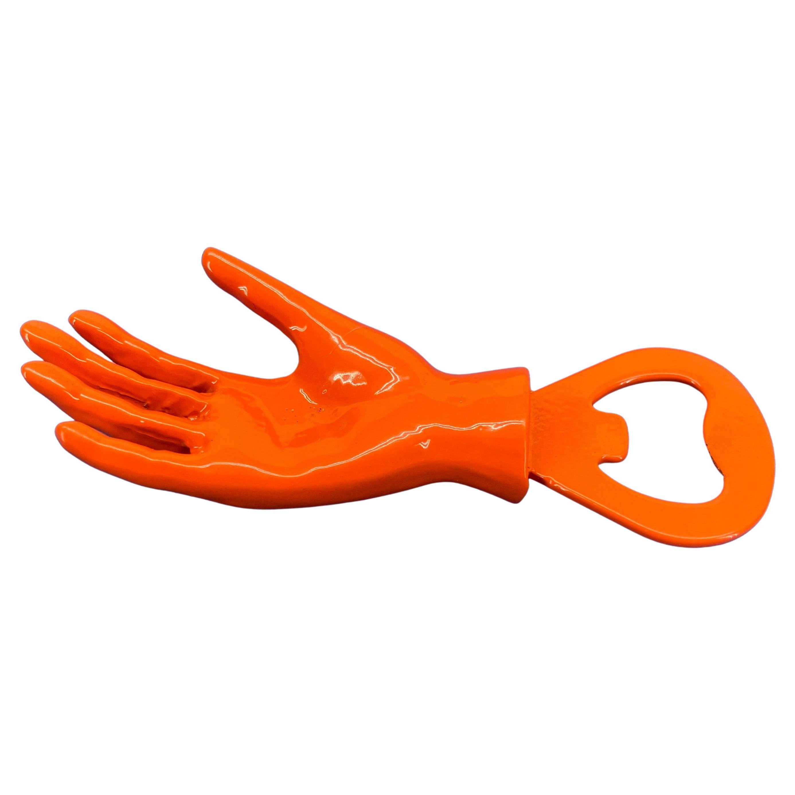 Modern bright orange powder coated cast iron bottle opener. In the shape of a hand, reminiscent of Fornasetti hands, this bright and bold bottle opener is sure to please in any bar setting. Small but mighty, the bottle opener will put a smile on