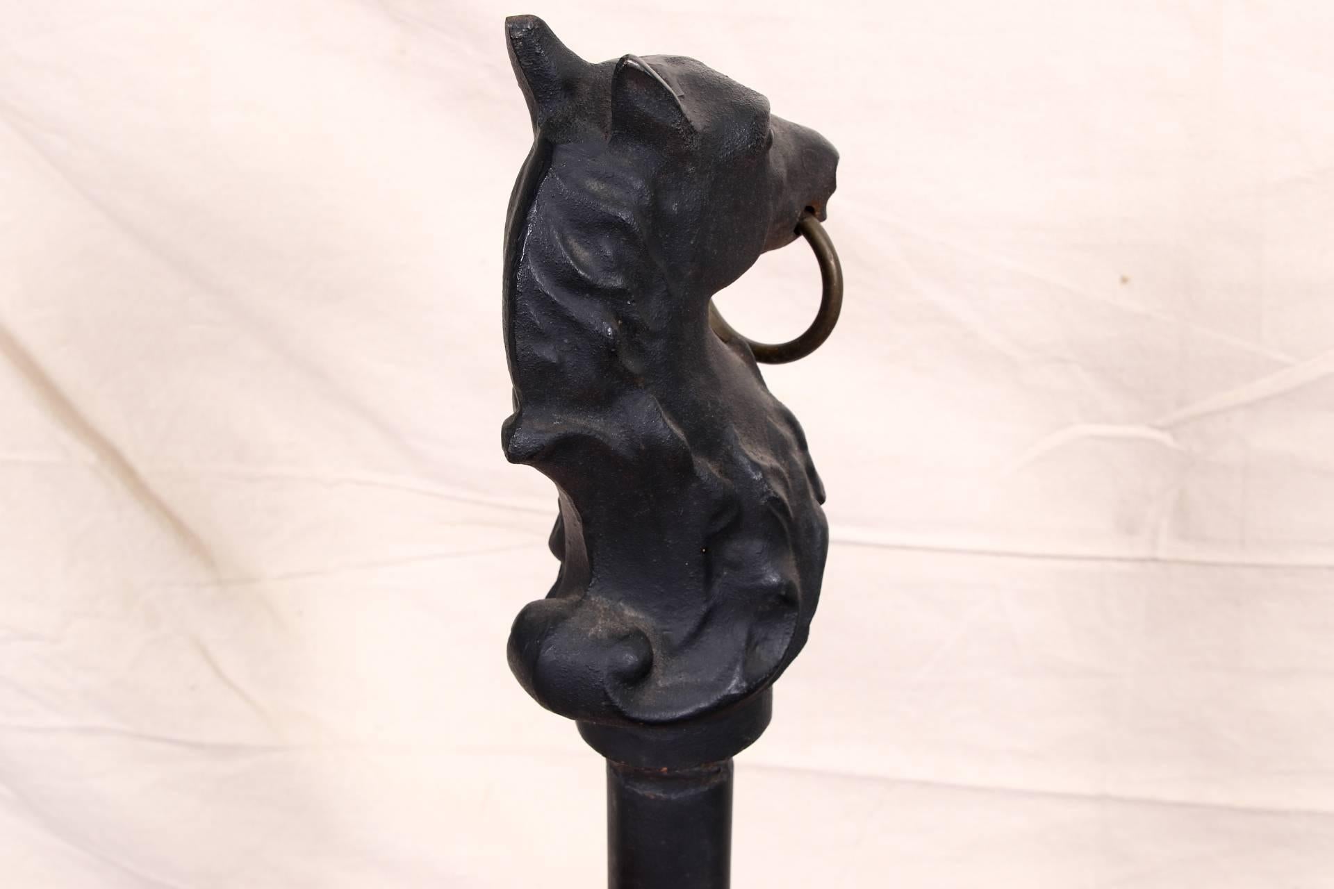 Cast iron hitching post with horse head, circa 1960s, black painted finish with a finely modeled horse head with scrolled leafy base and brass ring, mounted on a shaped Stand with a circular tiered base. 

Condition: Expected wear and signs of use