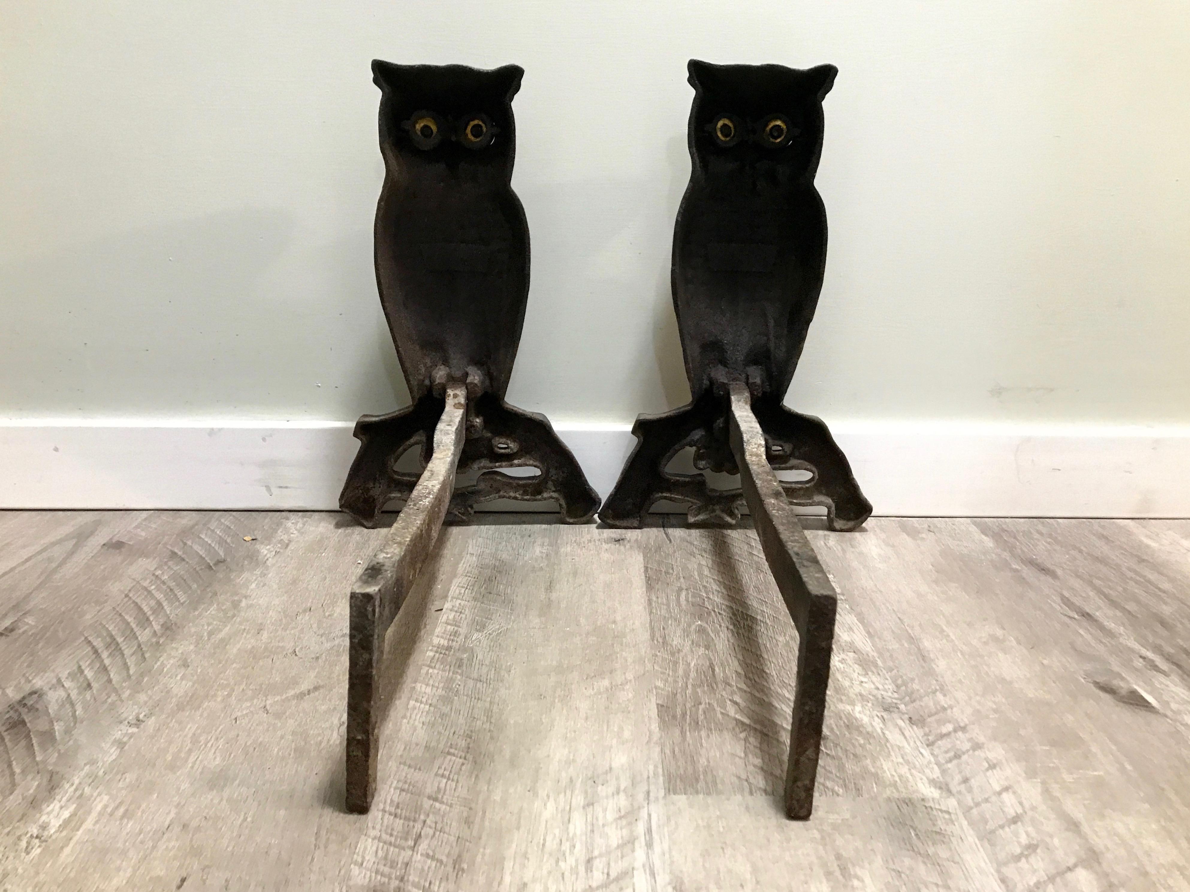Cast iron owl form andirons with glass eyes through which the fire glows. These were around the turn of the century (1900). The glass eyes are in tact with one small hairline crack, but not all the way through nor does it affect its functionality.