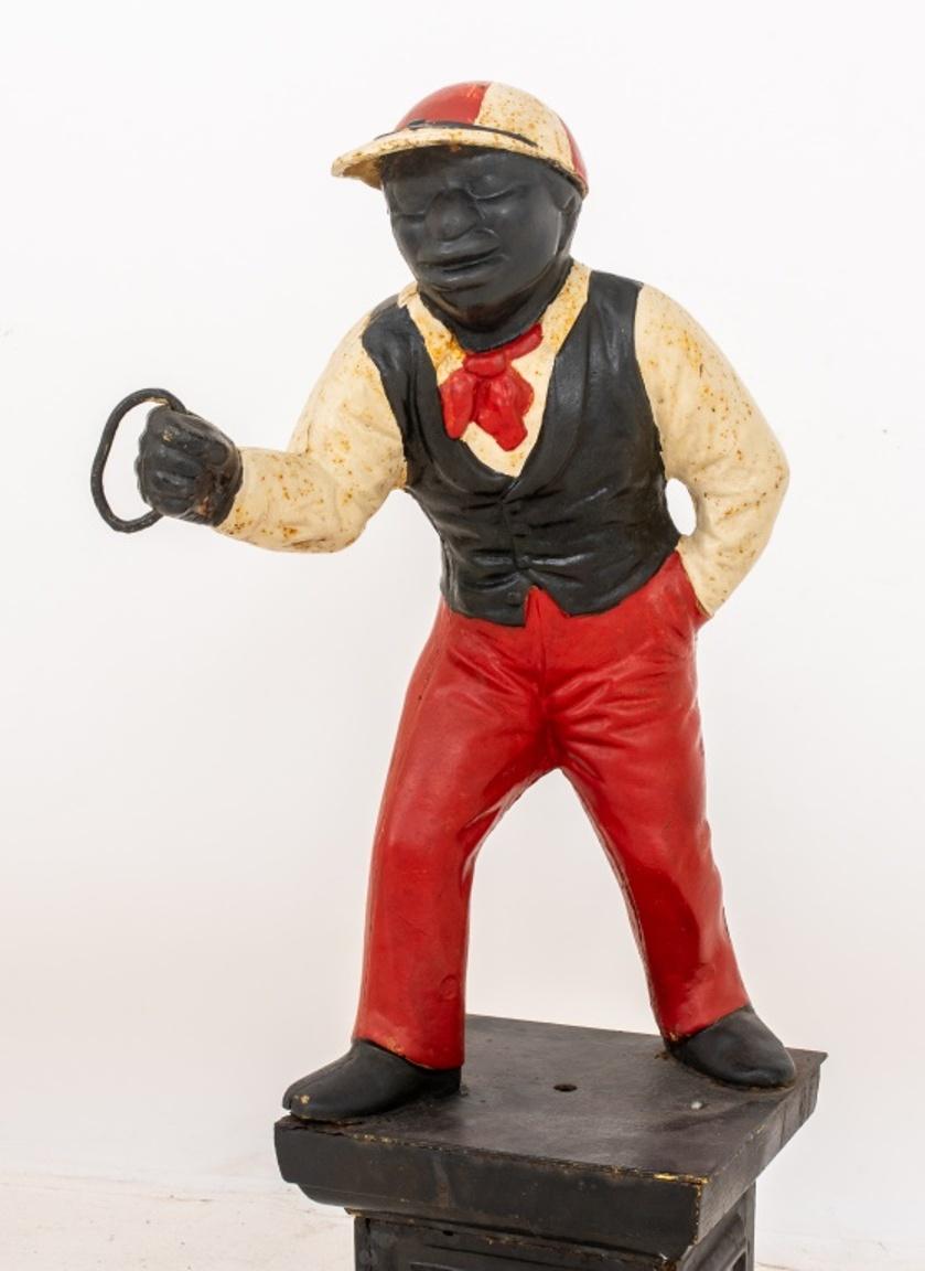 Cast Iron polychromed figural hitching post in the form of an African American jockey or groom wearing red white and black, standing on a black base. 37