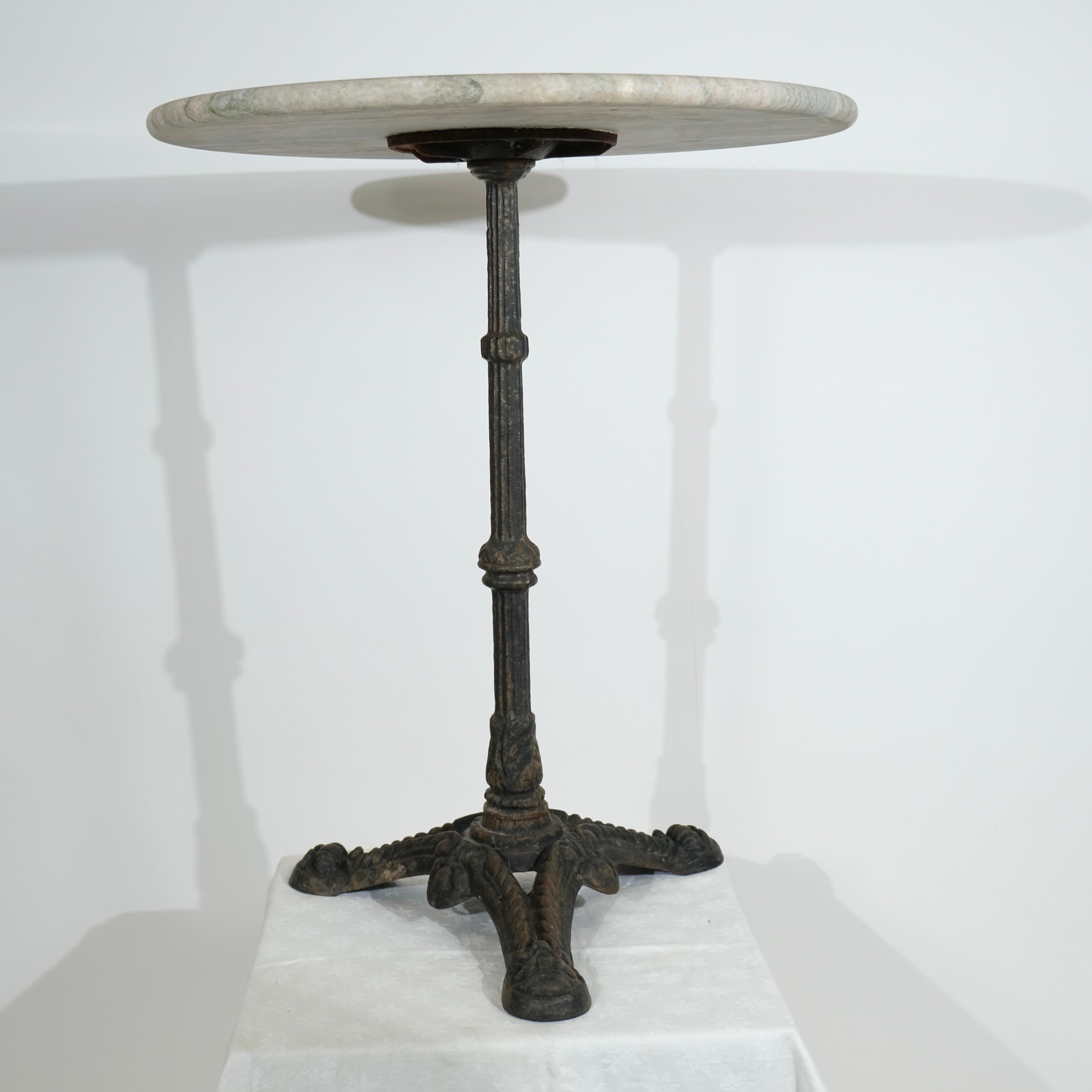 Cette exquise table ancienne, fabriquée au tournant du XXe siècle, est dotée d'une base en fonte joliment patinée et d'un élégant plateau en marbre. La base présente des détails complexes, avec des pieds ornés qui illustrent le savoir-faire de