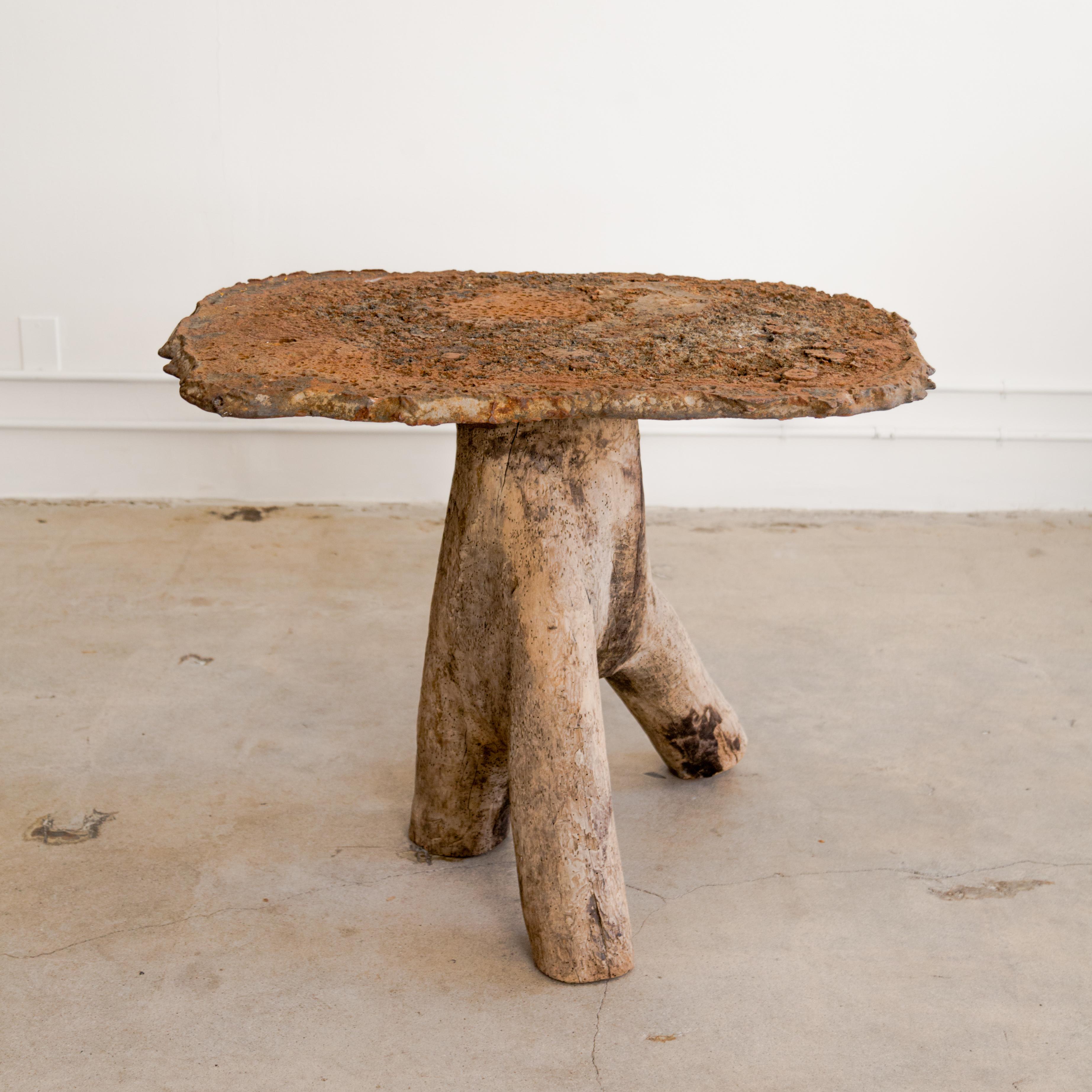Brutalist gueridon table with patinated cast iron top and tri-legged wood stump base.