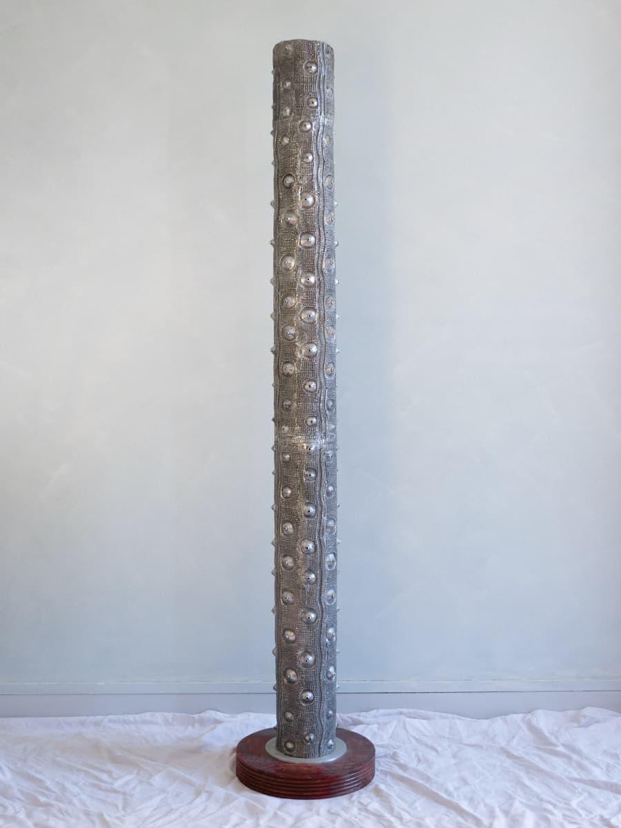 Floor lamp presented as a light column with cast aluminium nipples resting on a round wooden base, anonymous work from the 1990s.

This imposing luminous column with an offbeat aesthetic is like a real functional sculpture. The texture is put to
