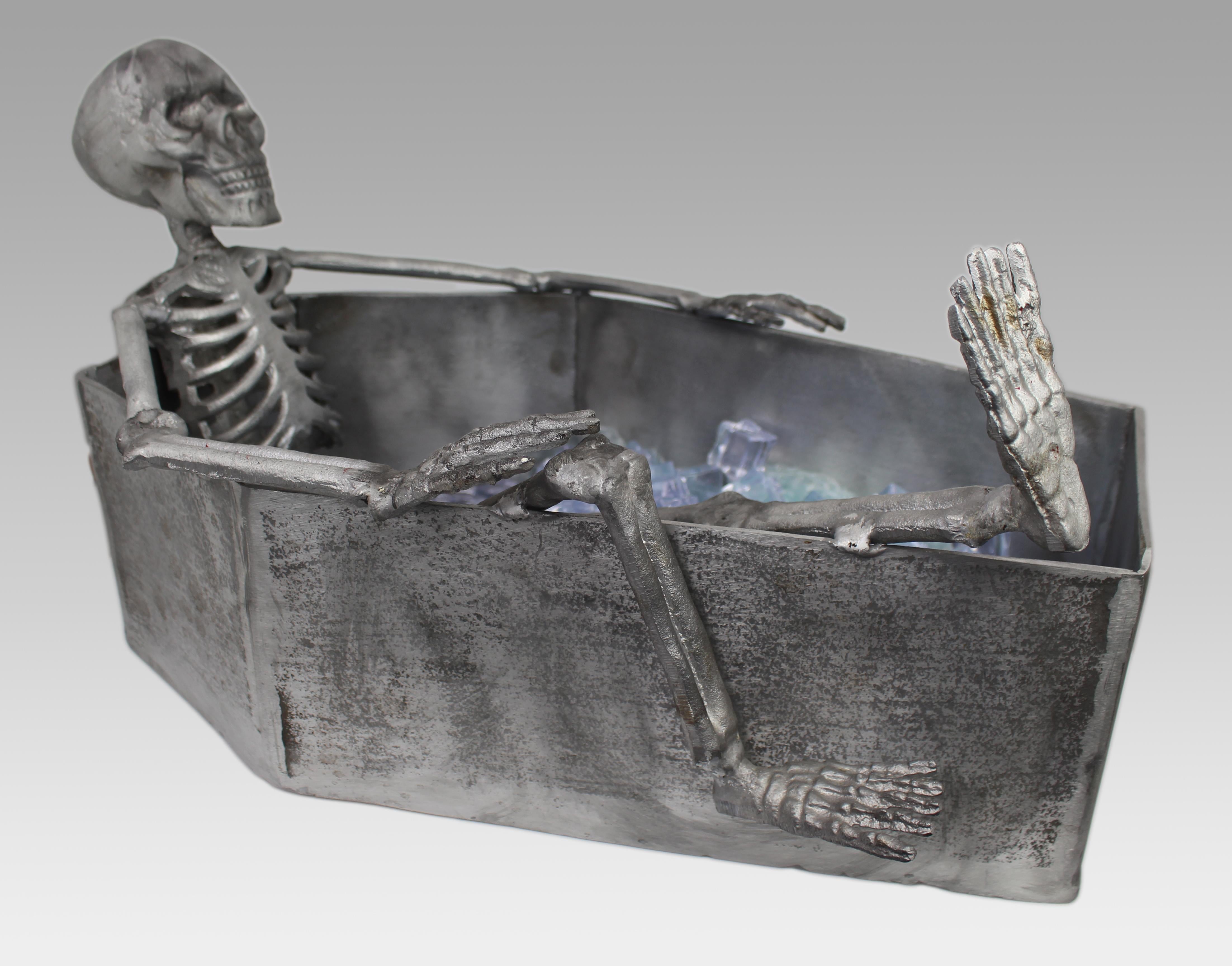 Cast Metal Skeleton Champagne Cooler in Coffin Form, c. 21st Century

A striking and surreal sculptural champagne cooler, cast entirely in metal and modelled as a reclining skeleton in a coffin-shaped vessel. This contemporary piece combines humour