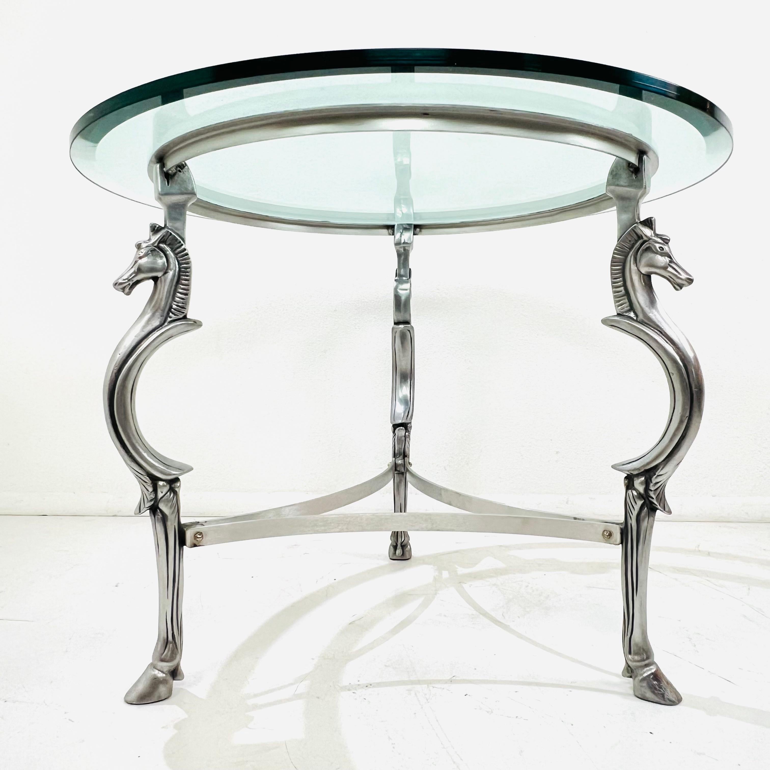 A modern classic with a sculptural twist — this round center table features a cast steel base with three stylized horse figures, each elegantly poised with arched necks and hooved feet beneath a thick glass top. The polished finish gives it a subtle