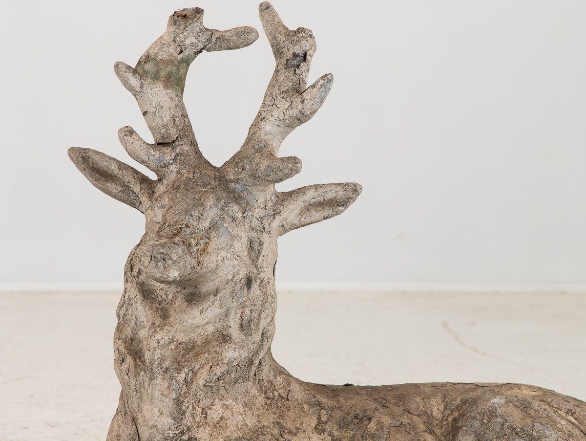 A late 19th century French cast stone buck or deer garden ornament. The style of this garden piece shows the buck lying down with its neck and head elevated. The front right leg is outstretched. This garden ornament retains much of its original
