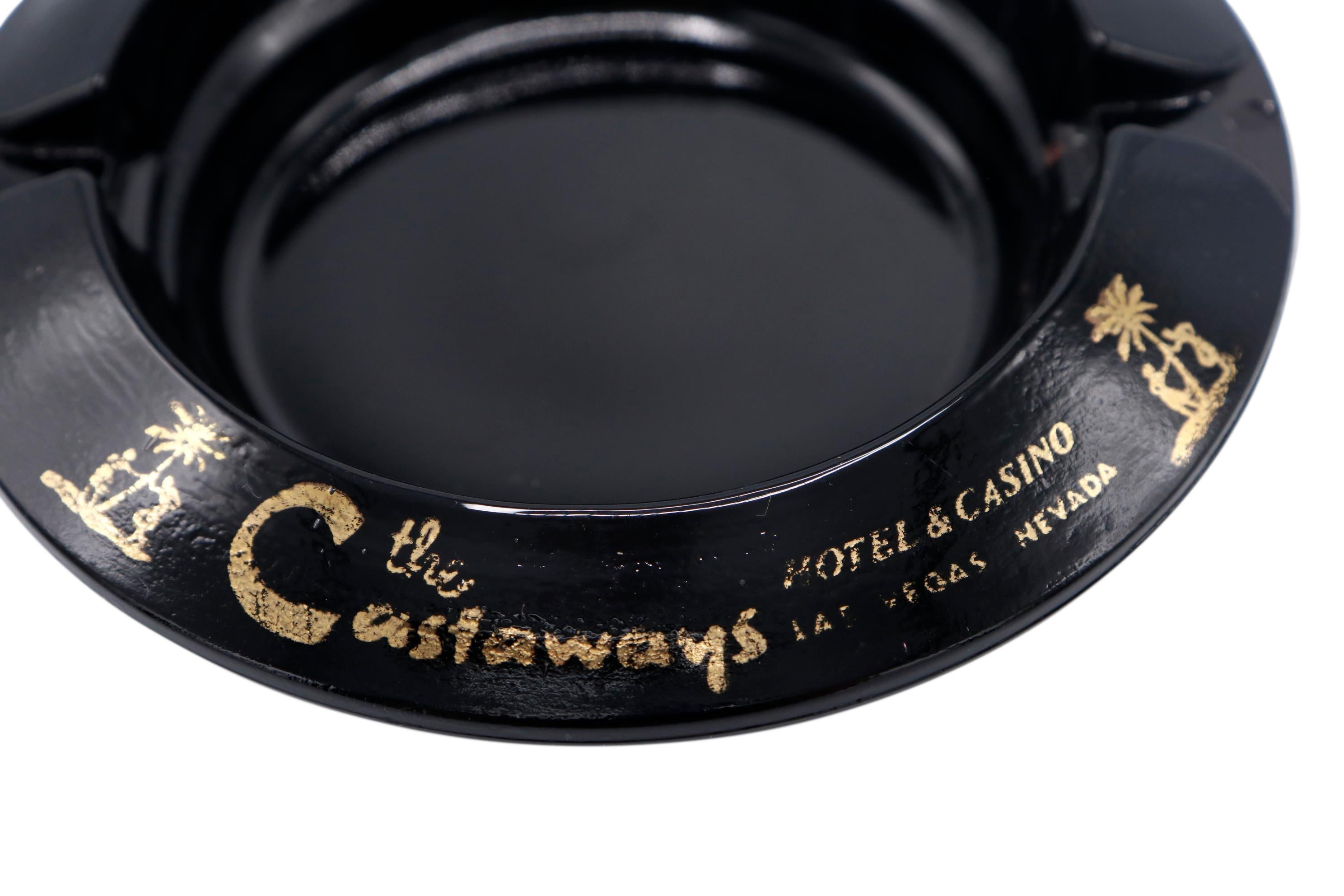 A black glass ashtray from The Castaways Hotel, a hotel and casino in Paradise, Las Vegas, Nevada. The lip is printed with the Castaways logo. The hotel, permanently closed in 1987, was opened in 1963 and purchased in 1967 by billionaire Howard
