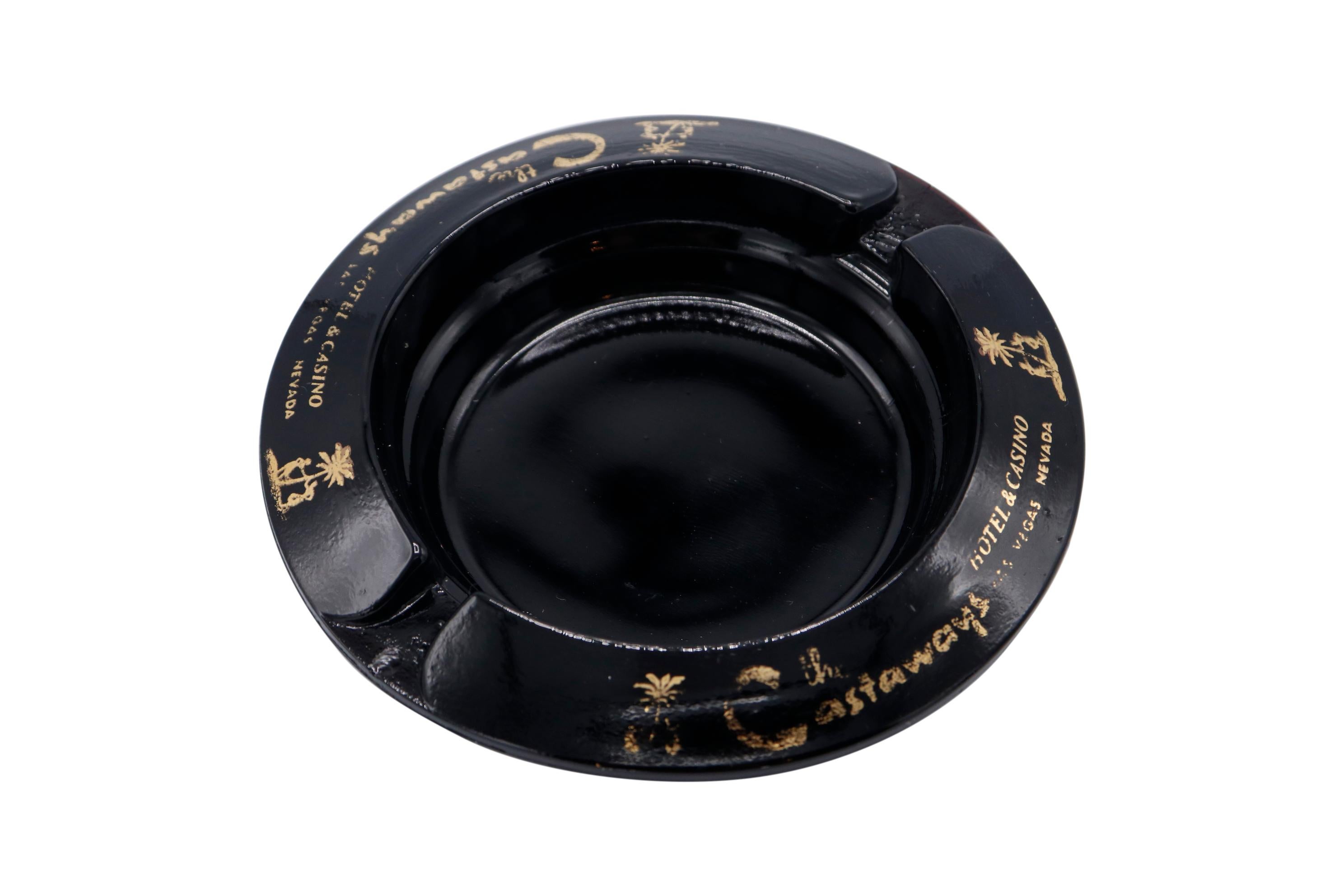A pair of black glass ashtrays from The Castaways Hotel, a hotel and casino in Paradise, Las Vegas, Nevada. The lip is printed with the Castaways logo. The hotel, permanently closed in 1987, was opened in 1963 and purchased in 1967 by billionaire