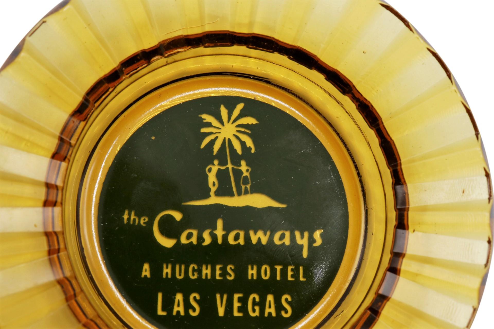 A yellow tinted glass ashtray from The Castaways Hotel, a hotel and casino in Paradise, Las Vegas, Nevada. The center is printed with a green circle branded with the Castaways logo. The hotel was opened in 1963, purchased in 1967 by billionaire