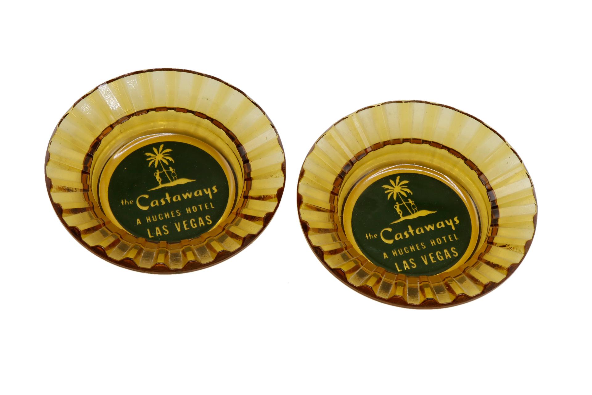 A pair of yellow tinted glass ashtrays from The Castaways Hotel, a hotel and casino in Paradise, Las Vegas, Nevada. The center is printed with a green circle branded with the Castaways logo. The hotel was opened in 1963, purchased in 1967 by