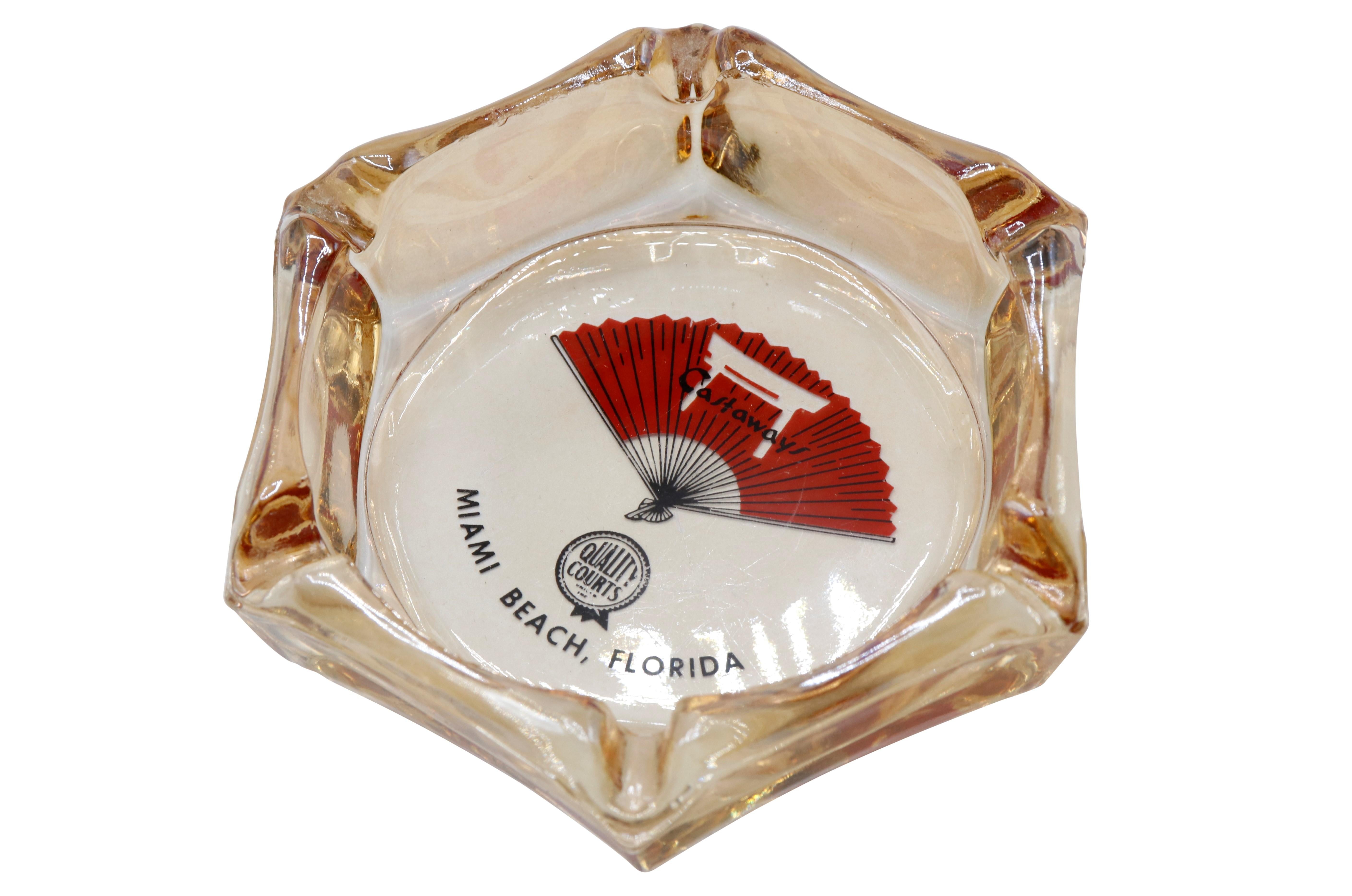A hexagonal glass ashtray from The Castaways Hotel of Miami Beach, Florida. The center is printed with their logo and reads “Castaways, Quality Courts, Miami Beach Florida”.
