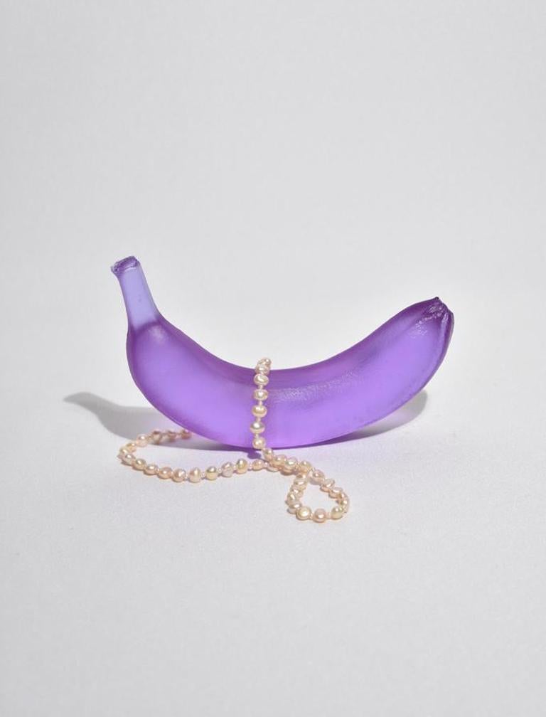 Casted glass banana in dichroic lilac by Devon Made inspired by blown glass fruit makers and collectors from the 1960's. The light playful approach to everyday fruit is contrasted with the heaviness of the crystal glass, a unique material that