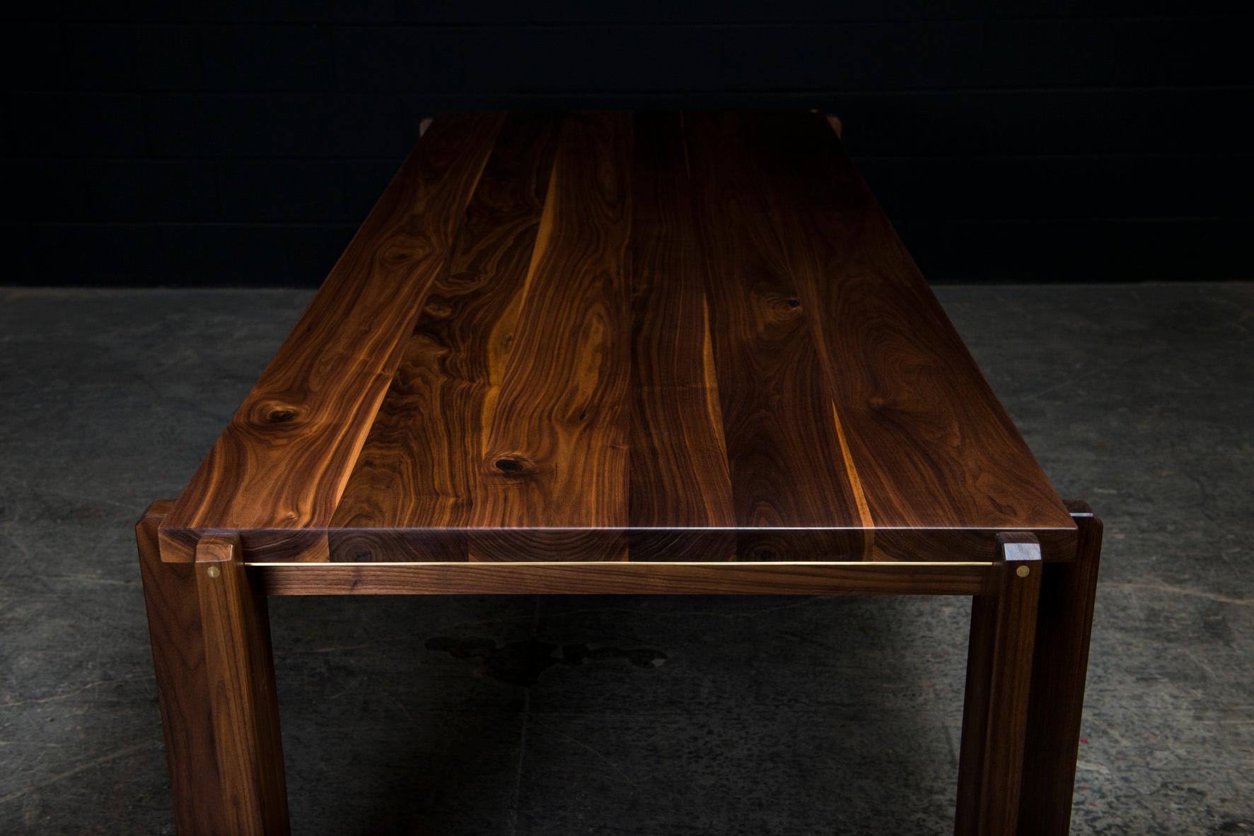 La Castelgar est une élégante table de salle à manger contemporaine fabriquée à la main sur commande à partir de bois dur américain massif sélectionné à la main, avec de subtils détails d'incrustation en laiton poli à la main. Les piliers en bois