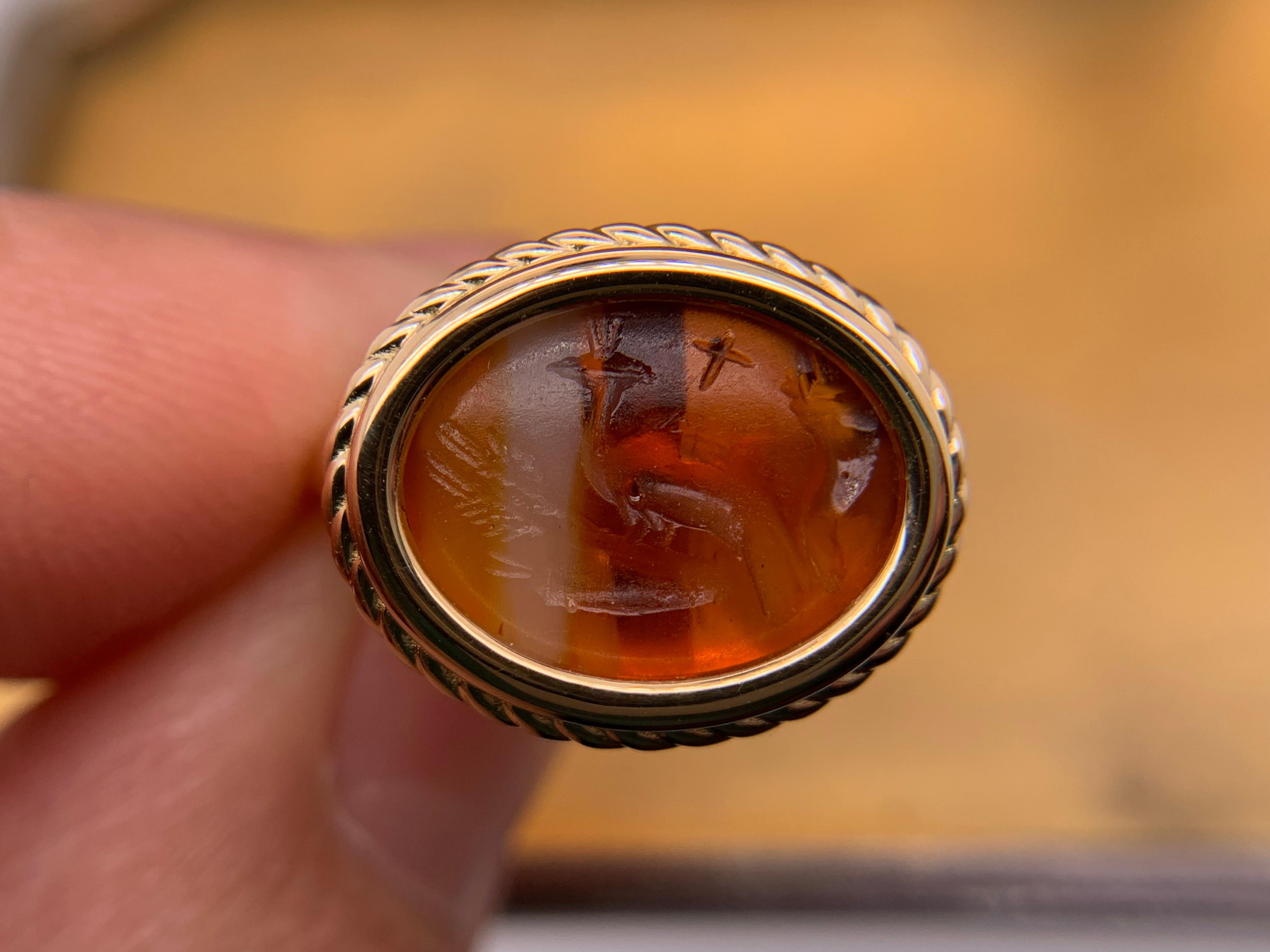 A lovely Ancient Roman gem. The orange and white banded agate intaglio is over 2000 years old. In tondo (carved on the horizontal), we find a peacock between two cornucopias and above it a cross. 
These three Ancient Roman symbols carved into this