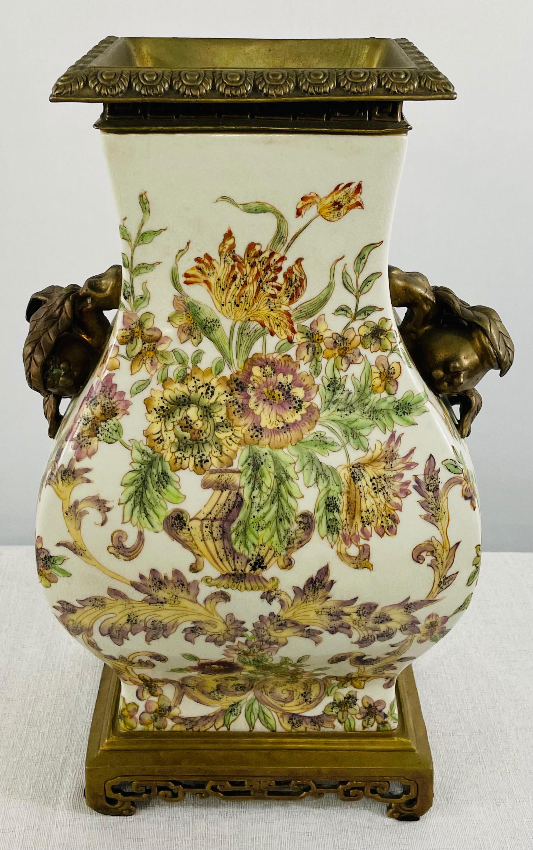 A 20th Century Castilian porcelain vase featuring exquisite floral design in Green, yellow and purple tone on a white background. The elegant vase is embellished with bronze inlay around the mouth of the vase and two bronze handles each in the form