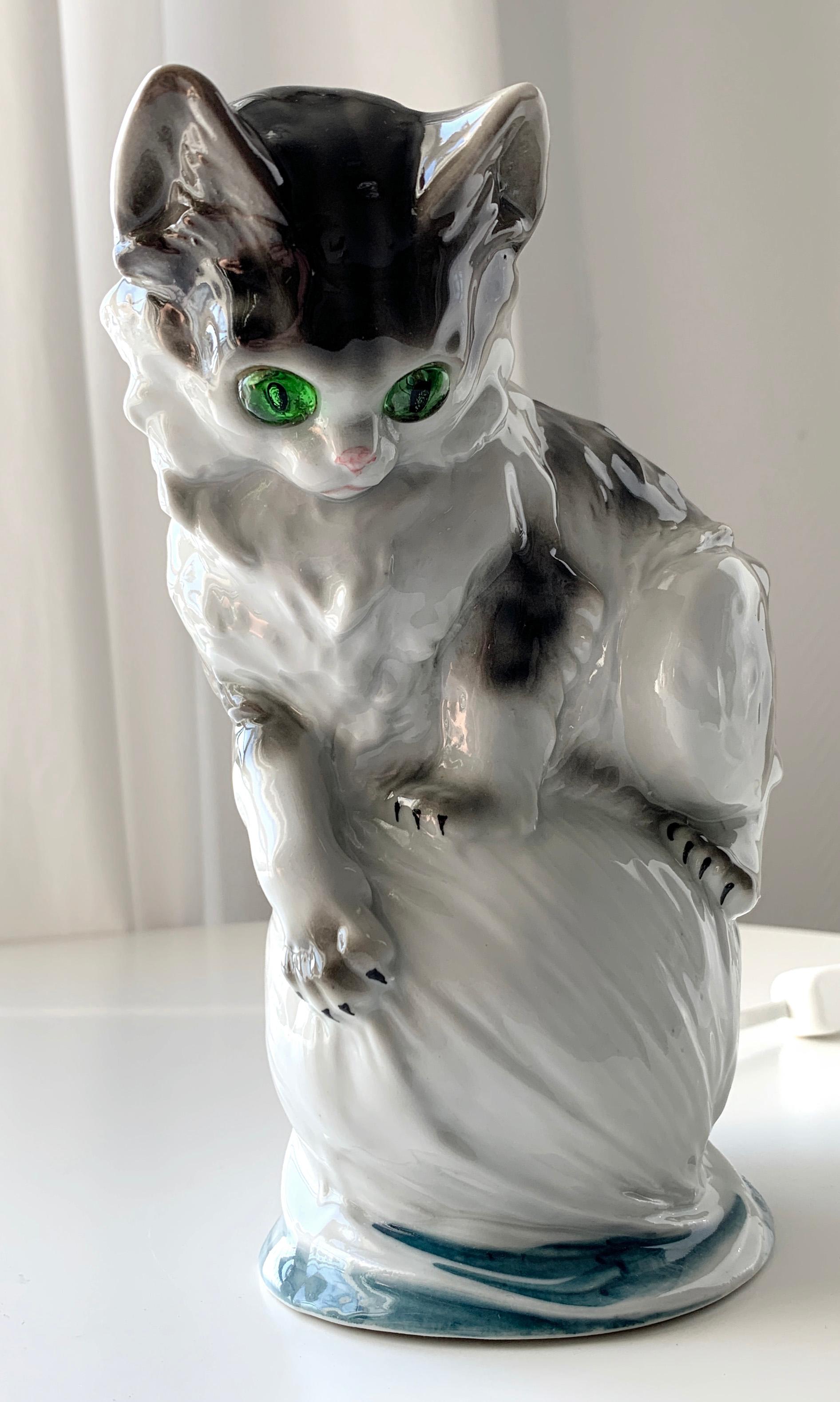 Figurine porcellain lamp with cat balancing on a yarn nest. Early 20th century ozon table lamp. White porcelain hand painted with joyful colors. Electrically mounting could be done by Danish Fog & Mørup. Similar figurines seens as a series of