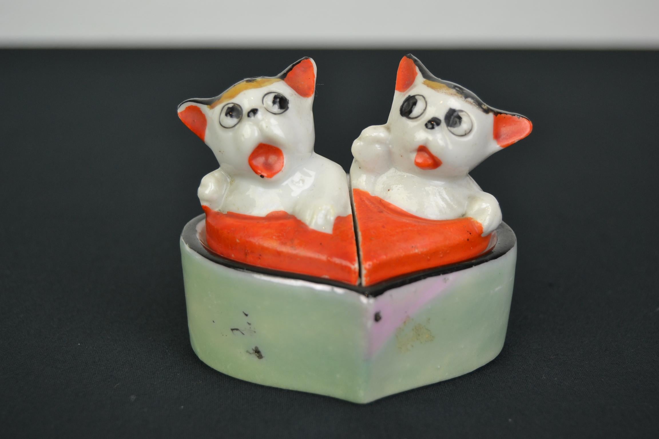 This is a set for a cat lover: 
Salt and pepper shaker set combined with mustard pot. 
Two cats ( salt and pepper shakers ) seated on a heart shaped - mustard pot. 
It's glazed hand-painted porcelain in the style of the Bonzo caricatures.