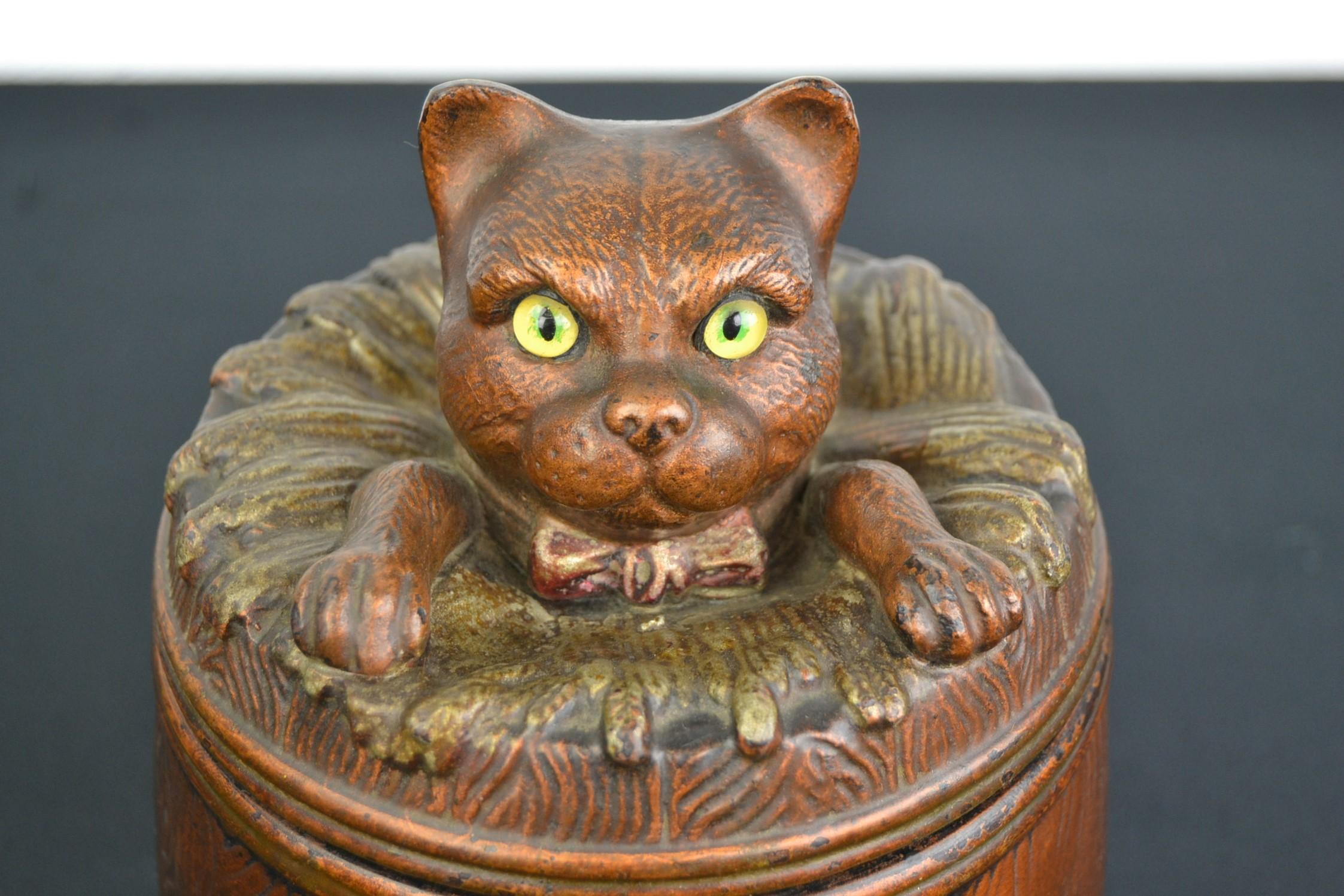 Tobacco jar with cat or puss on top of the lid. 
This tobacco jar in the shape of a barrel looks great ! 
The cat who peeps out of the barrel has yellow glass eyes, wears a bow around the neck and leans on his 2 front paws on the barrel.
This